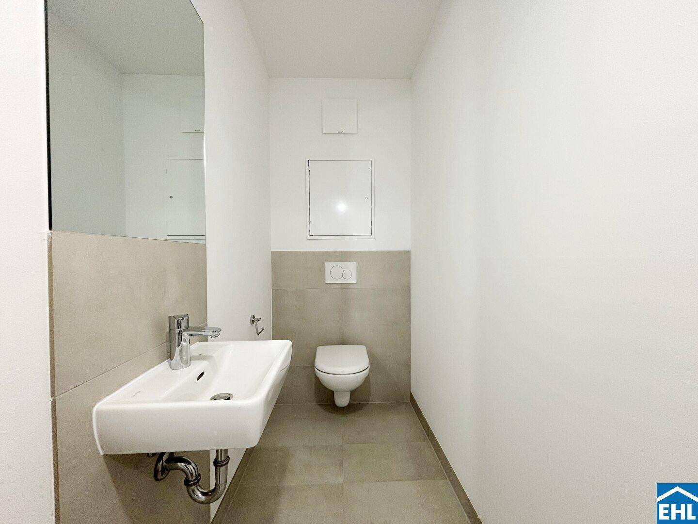 Separates WC mit wandhängender Toilette, kleinem Waschbecken und modernen Fliesen.