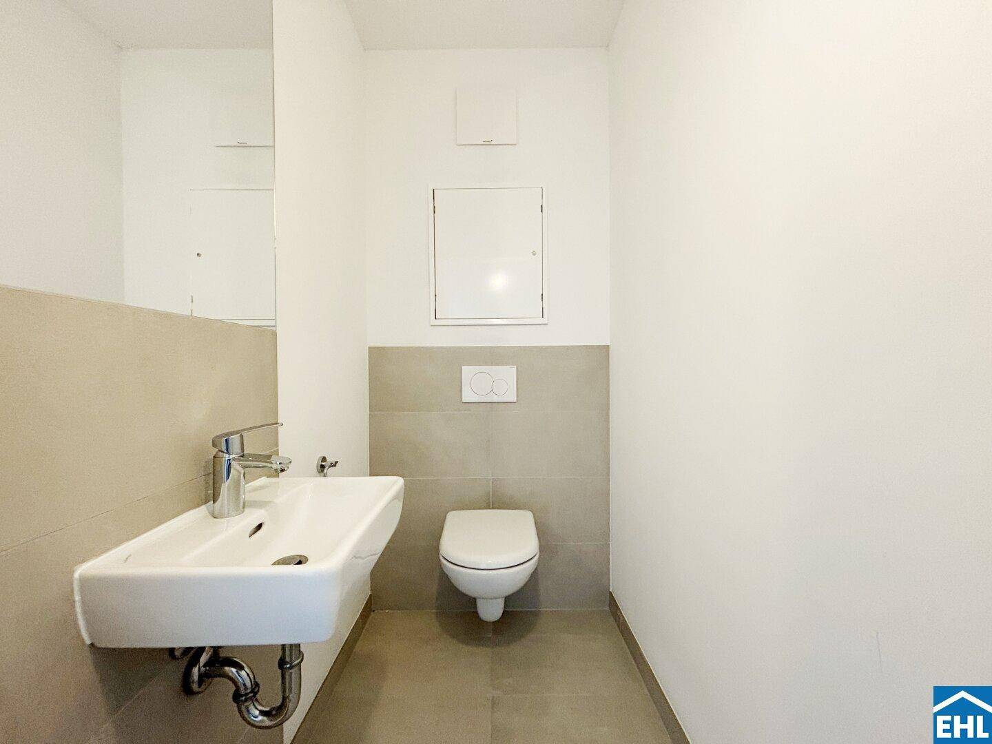 Separates Gäste-WC mit wandhängender Toilette, kleinem Waschbecken und modernen Fliesen.