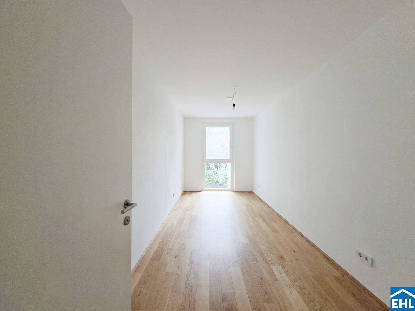 Helles Zimmer mit Holzboden und großem Fenster, ideal als Schlaf- oder Arbeitszimmer.