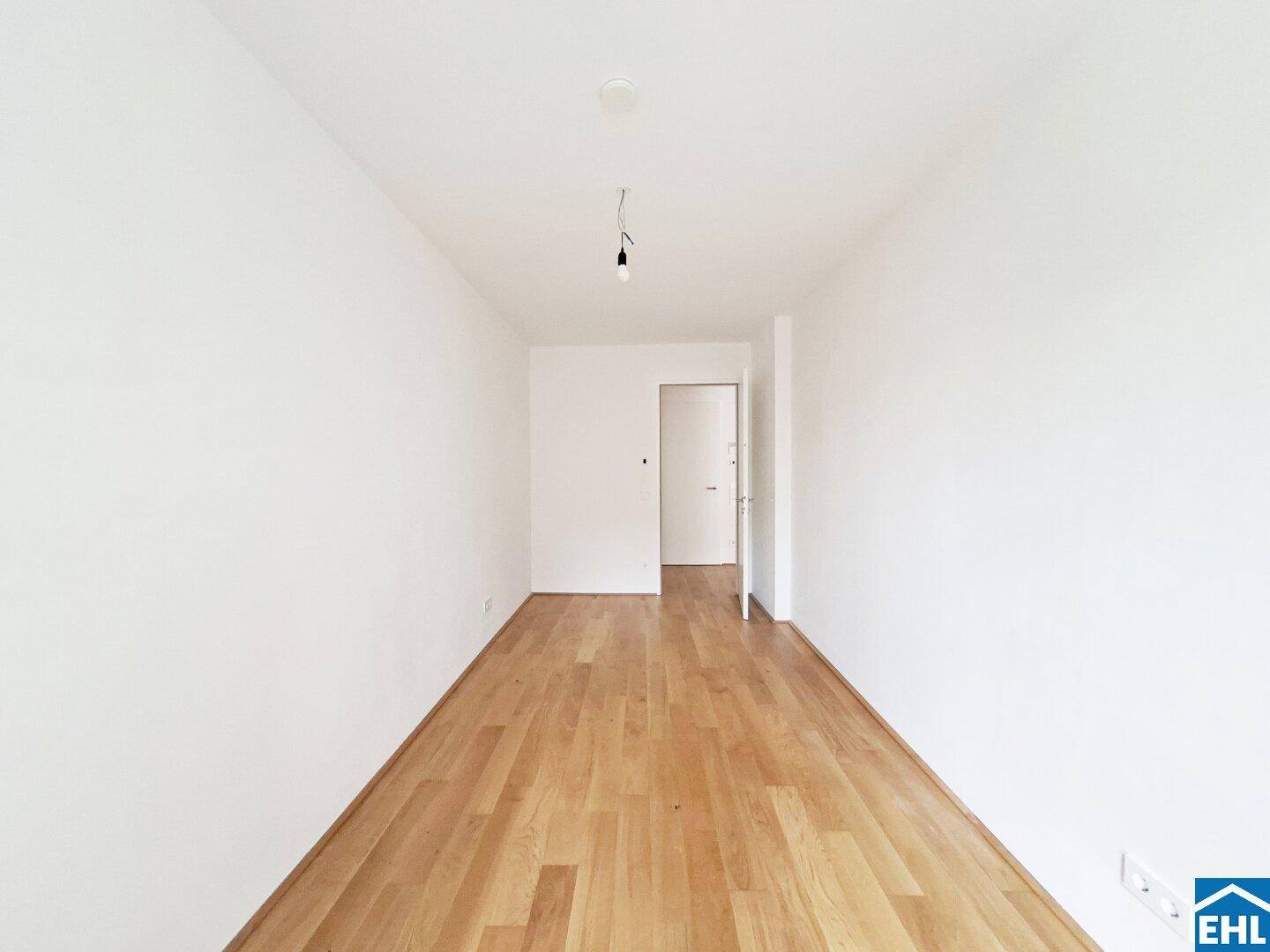 Leeres Zimmer mit Holzboden und weiß gestrichenen Wänden, bereit zum Einzug.