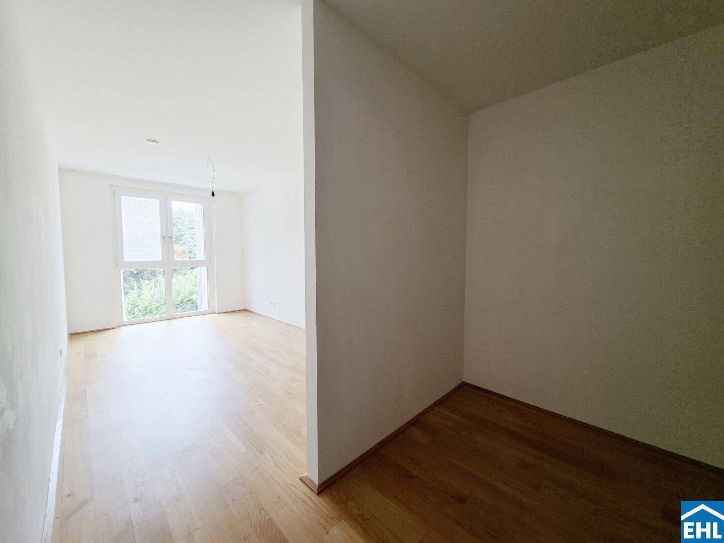 Heller Flur mit Holzboden, der zu einem weiteren Zimmer mit Fenster führt.