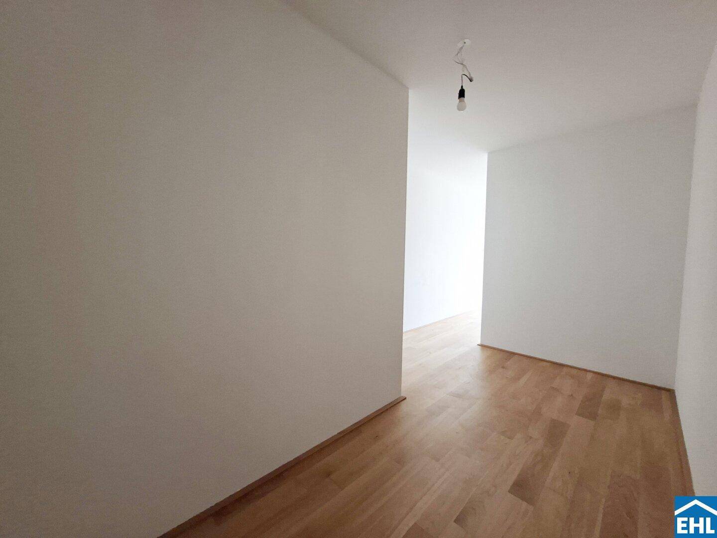 Schlichter Flur mit Holzboden und weißen Wänden, der den Wohnbereich verbindet.