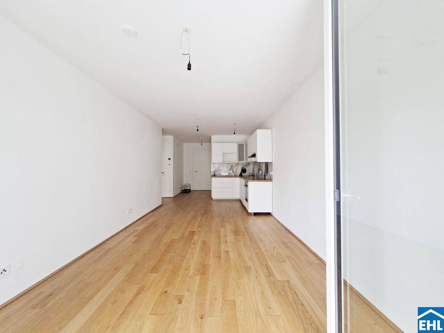 Geräumiger offener Wohnbereich mit heller Küche und durchgehendem Holzboden, viel Tageslicht.