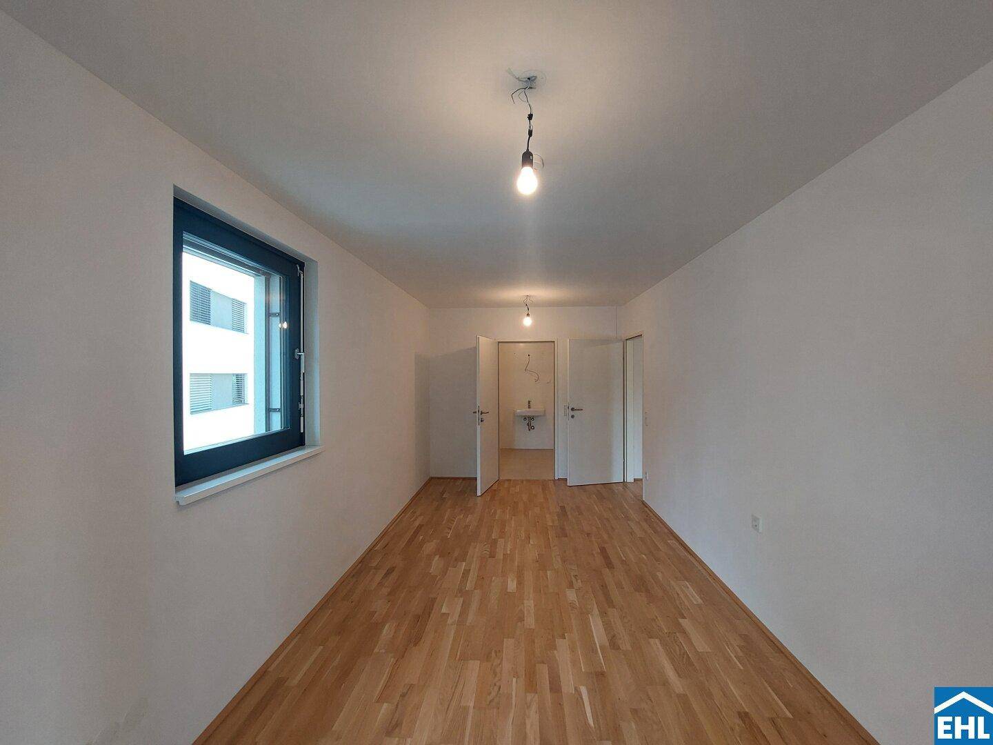 Geräumiges Zimmer mit Parkettboden, großem Fenster und direktem Zugang zu einem angrenzenden Badezimmer.