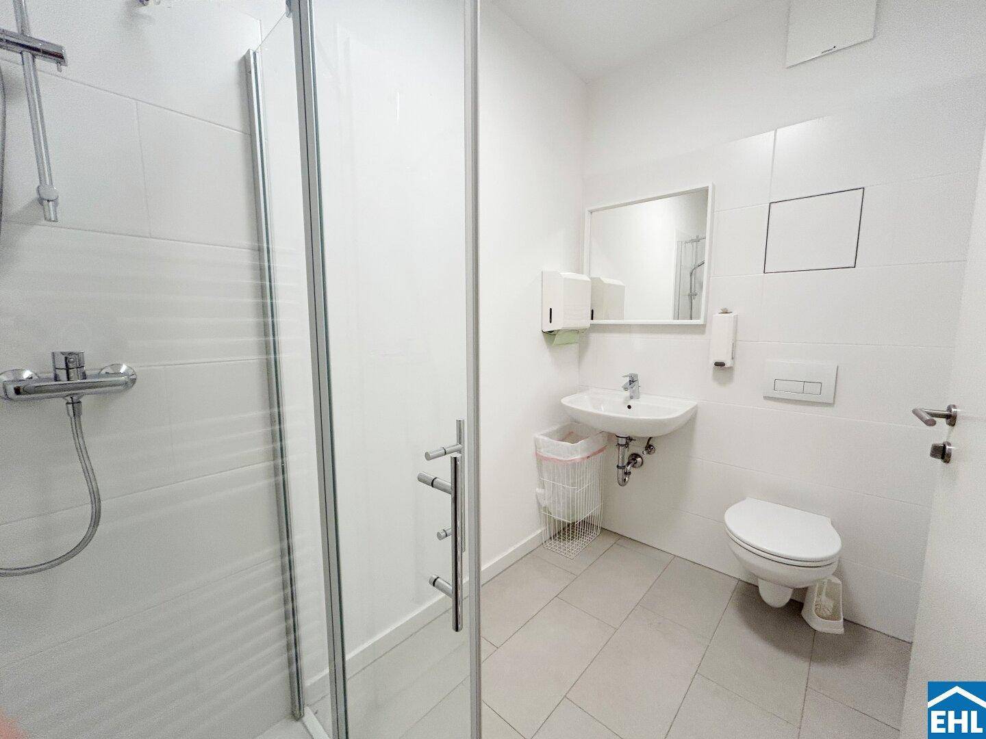 Modernes Badezimmer mit Dusche, Waschbecken und WC, in hellen Fliesen gehalten.