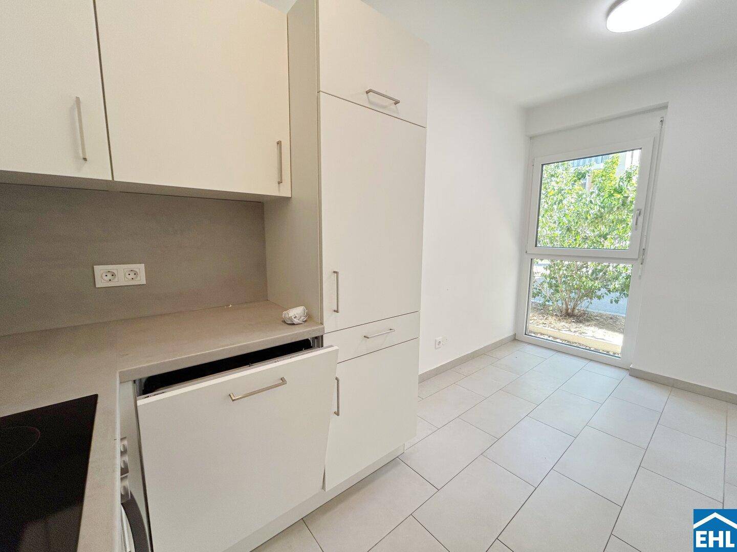 Moderne Einbauküche mit hellen Schränken, integrierten Geräten und Fenster für Tageslicht.