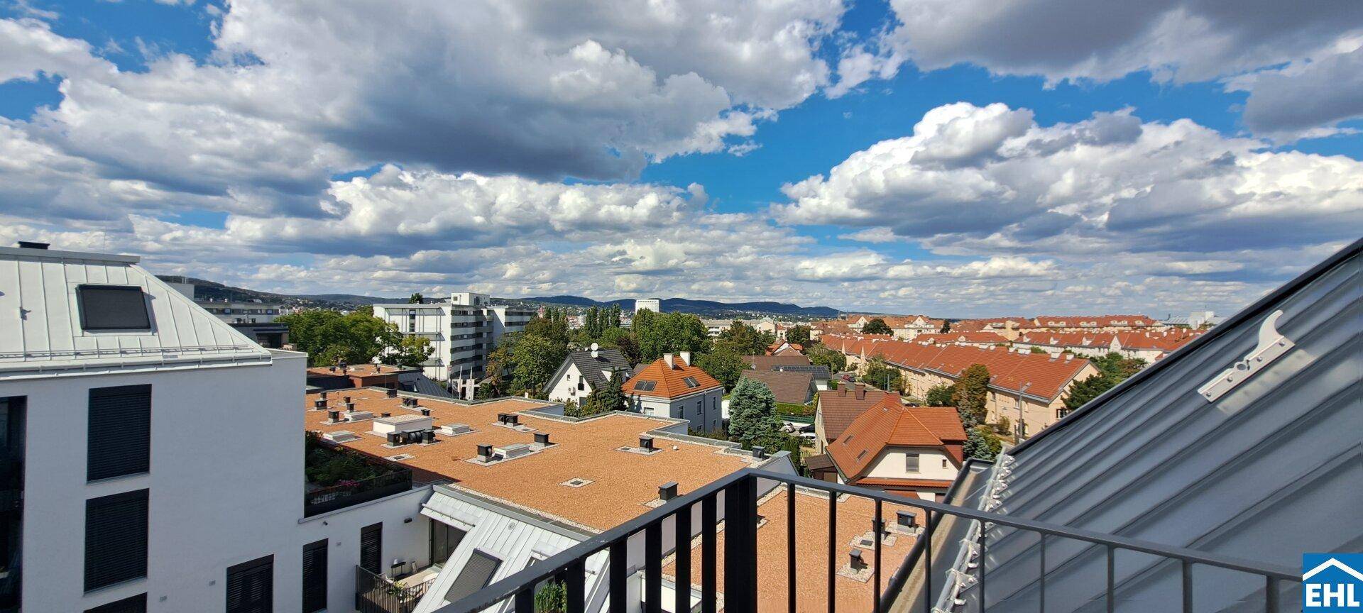 Blick von einem Balkon über die Dächer der Stadt mit grünen Hügeln im Hintergrund.