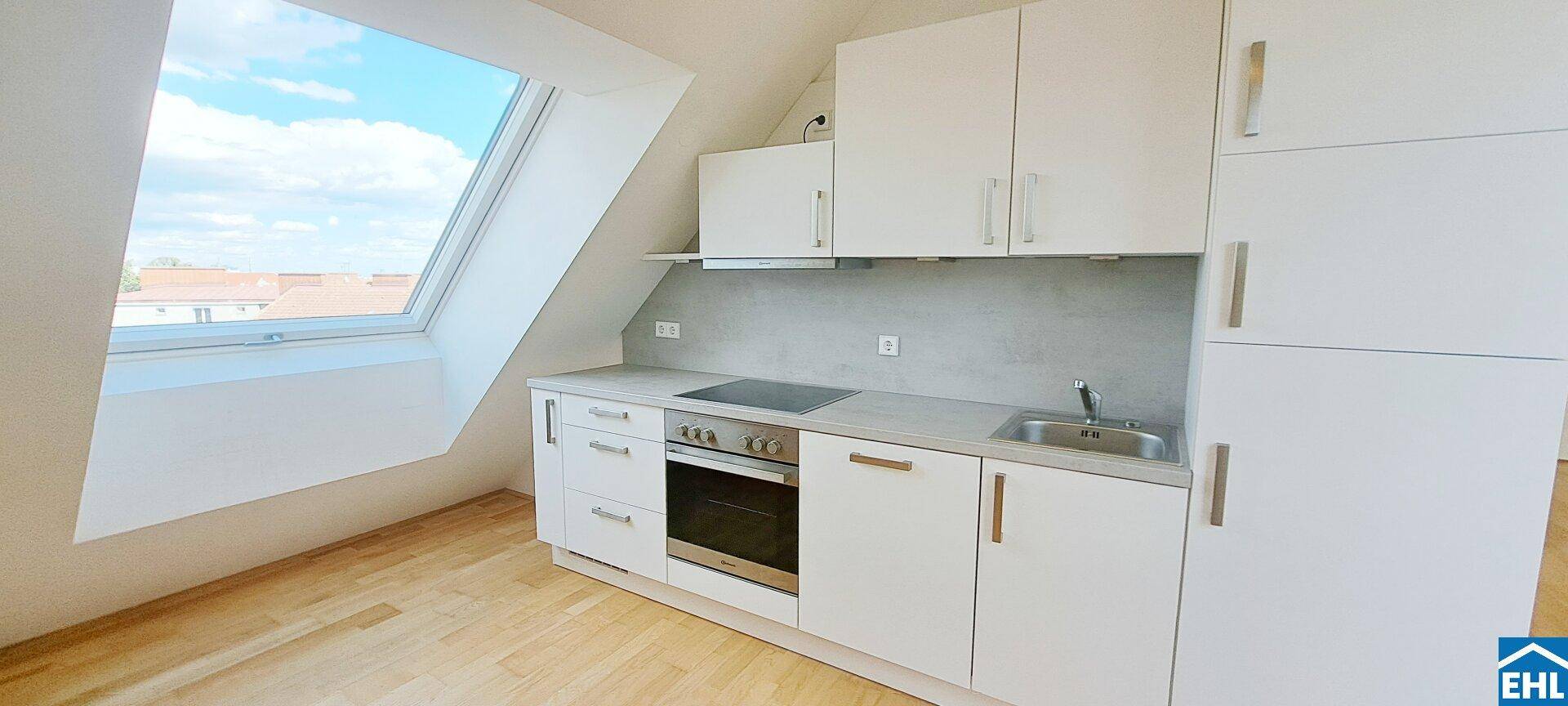 Kompakte Einbauküche mit weißen Fronten, Kochfeld und Backofen unter einem Dachfenster.