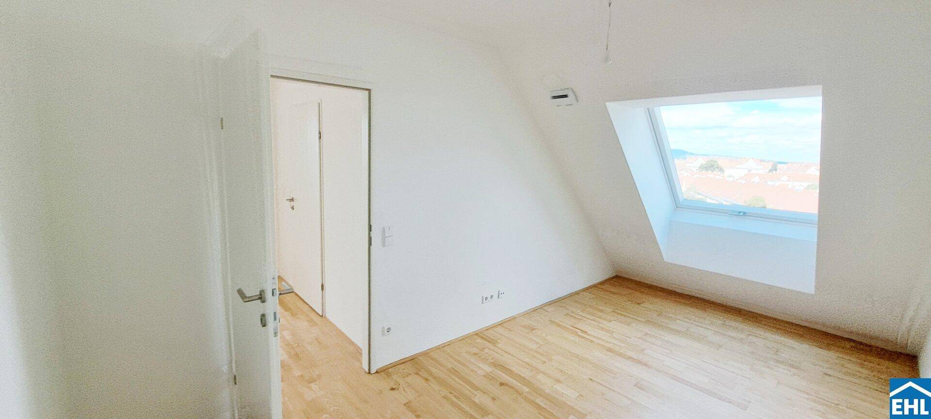 Leeres Zimmer im Dachgeschoss mit Holzboden, Dachschräge und hellem Fenster.