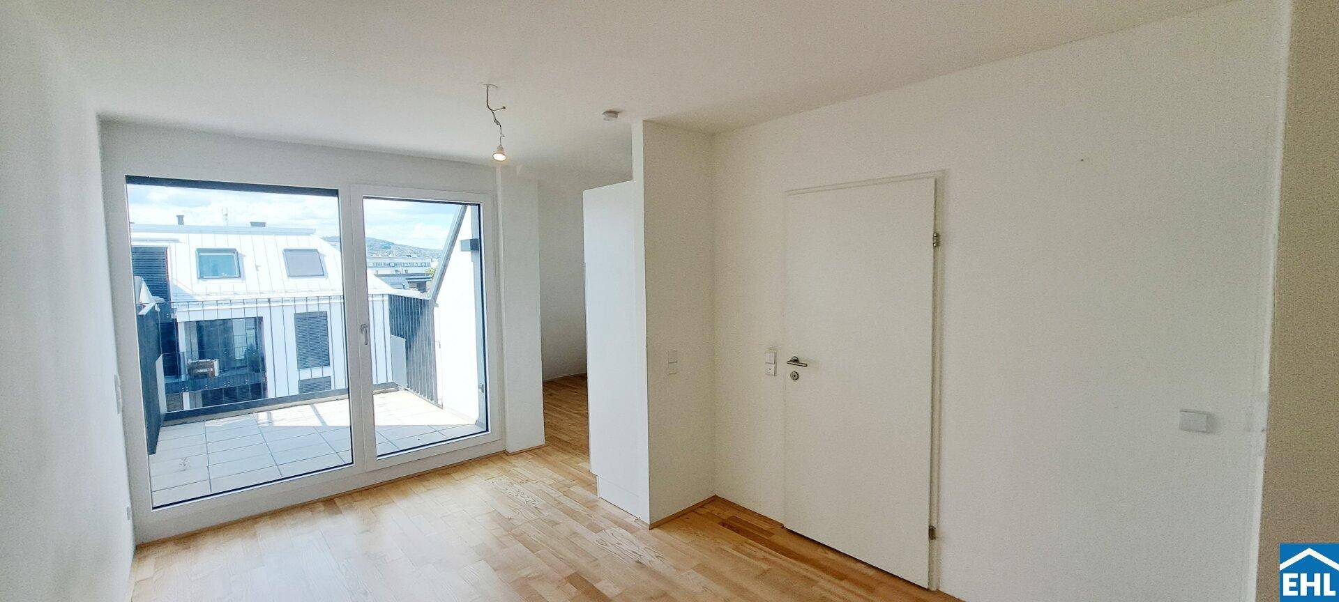Heller Wohnraum mit Zugang zu einem Balkon und schrägen Wänden im Dachgeschoss.
