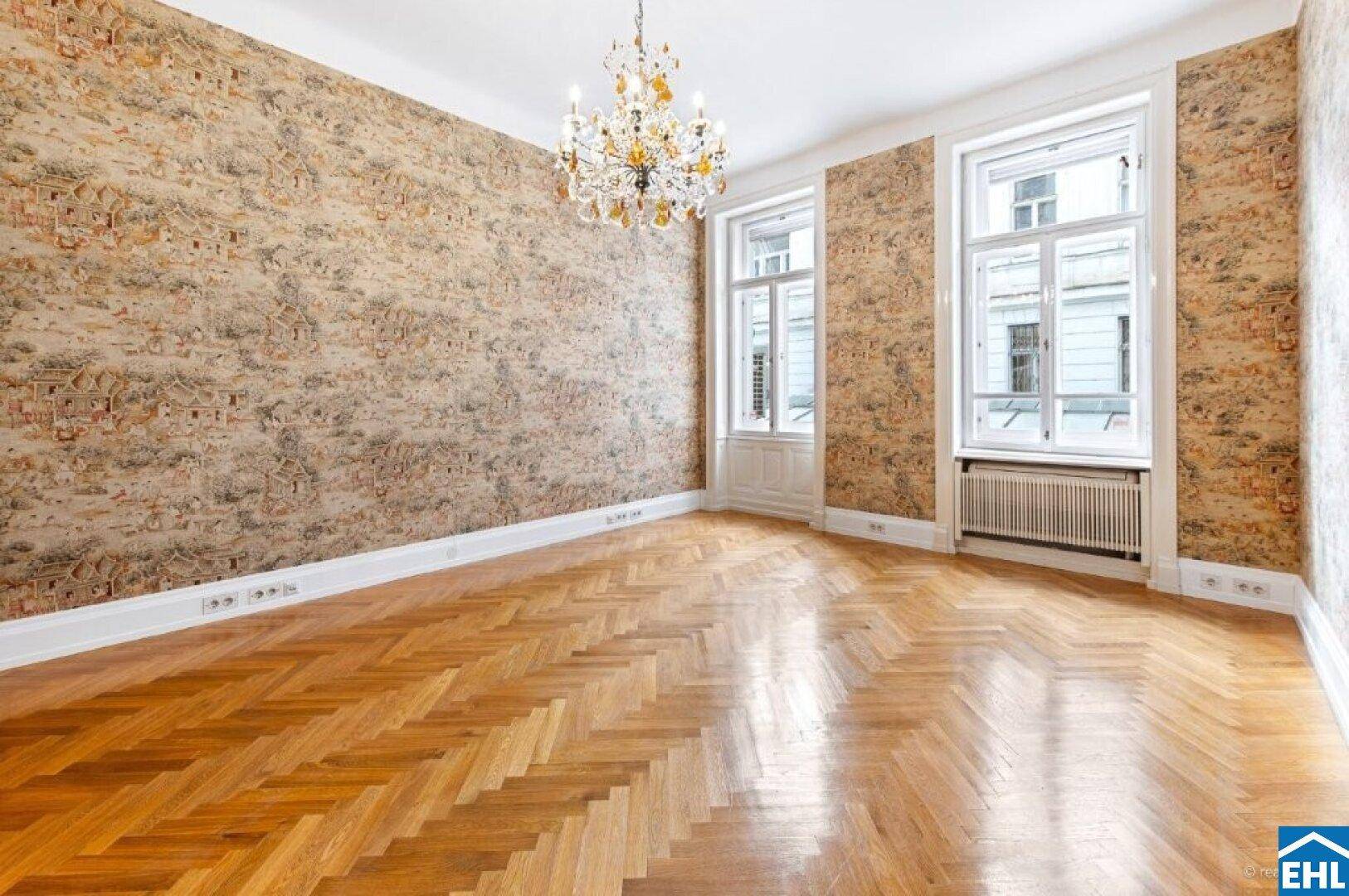 Heller Raum mit gemusterter Tapete, Fischgrätparkett und einem eleganten Kronleuchter.