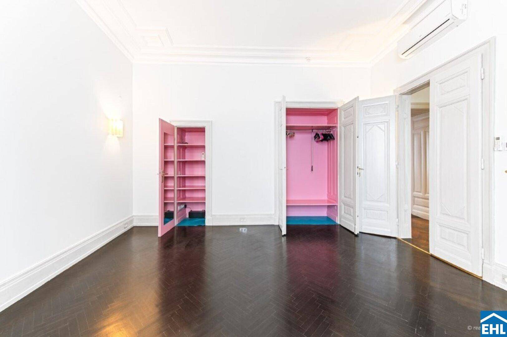 Heller Raum mit dunklem Fischgrätparkett und offenen pinken Einbauschränken.
