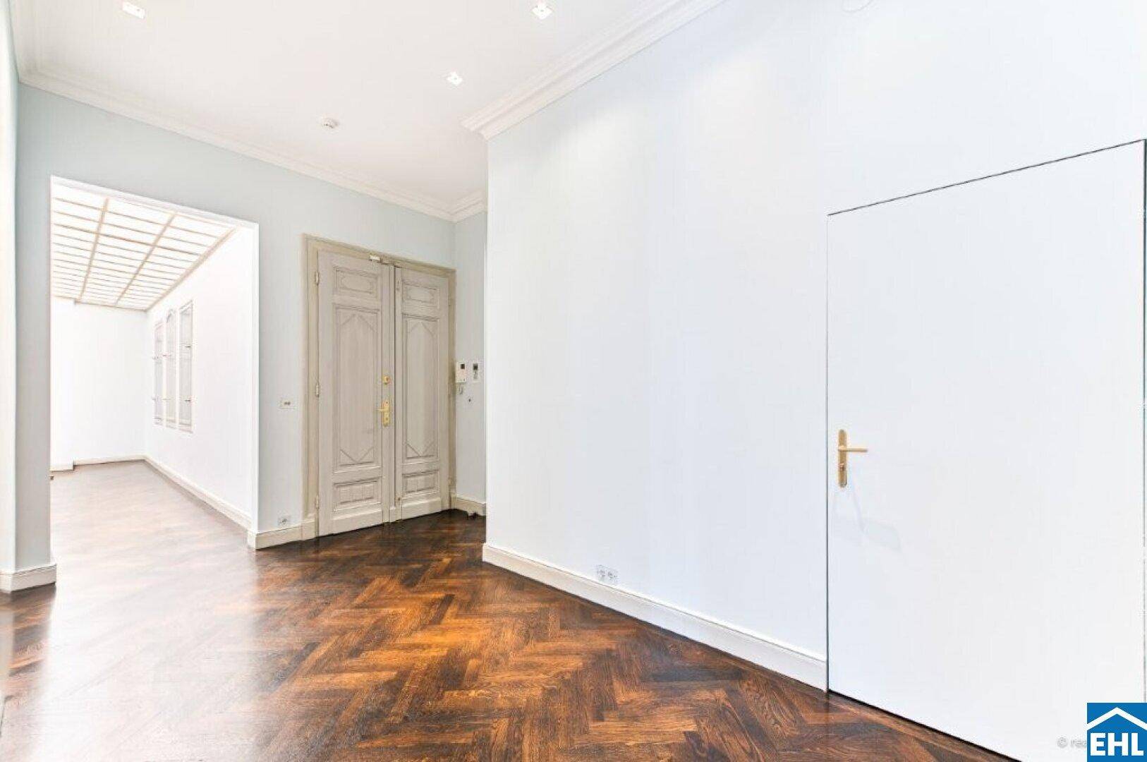Geräumiger Flur mit dunklem Fischgrätparkett und eleganten Doppeltüren.