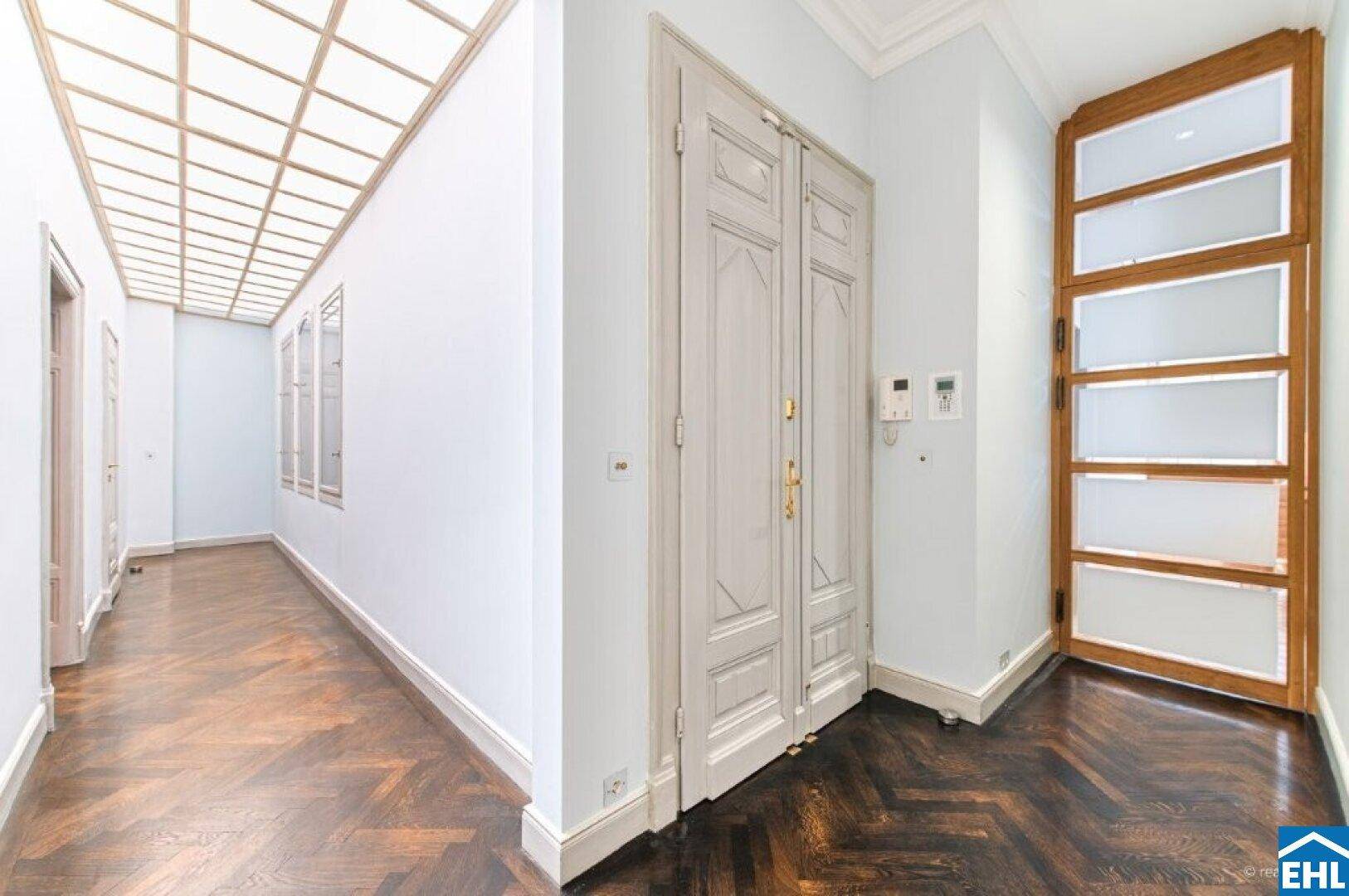 Langer Flur mit dunklem Fischgrätparkett, Kassettendecke und eleganten Türen.