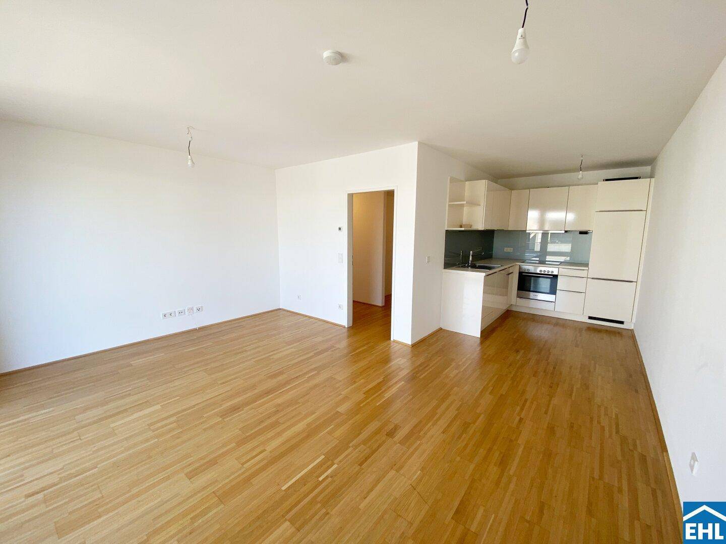 Offener Wohn- und Essbereich mit integrierter Küche und hellem Holzparkett, ideal für modernes Wohnen.