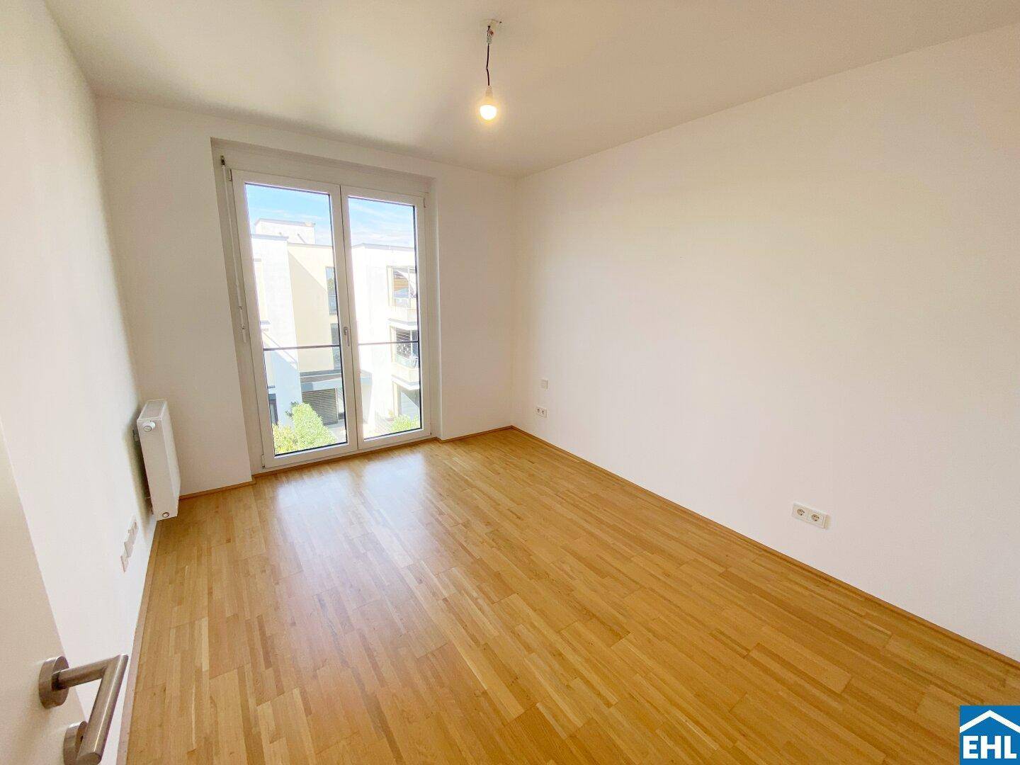 Schlafzimmer mit Zugang zu einem Balkon und hellem Holzfußboden, bietet viel Tageslicht.