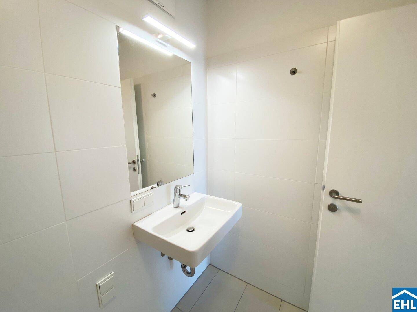 Modernes Badezimmer mit weiß gefliesten Wänden, Waschbecken und großem Spiegel.