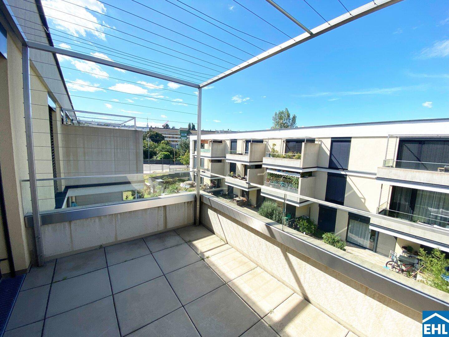 Geräumiger Balkon mit Fliesenboden und Blick auf die umliegenden Gebäude und Grünflächen.