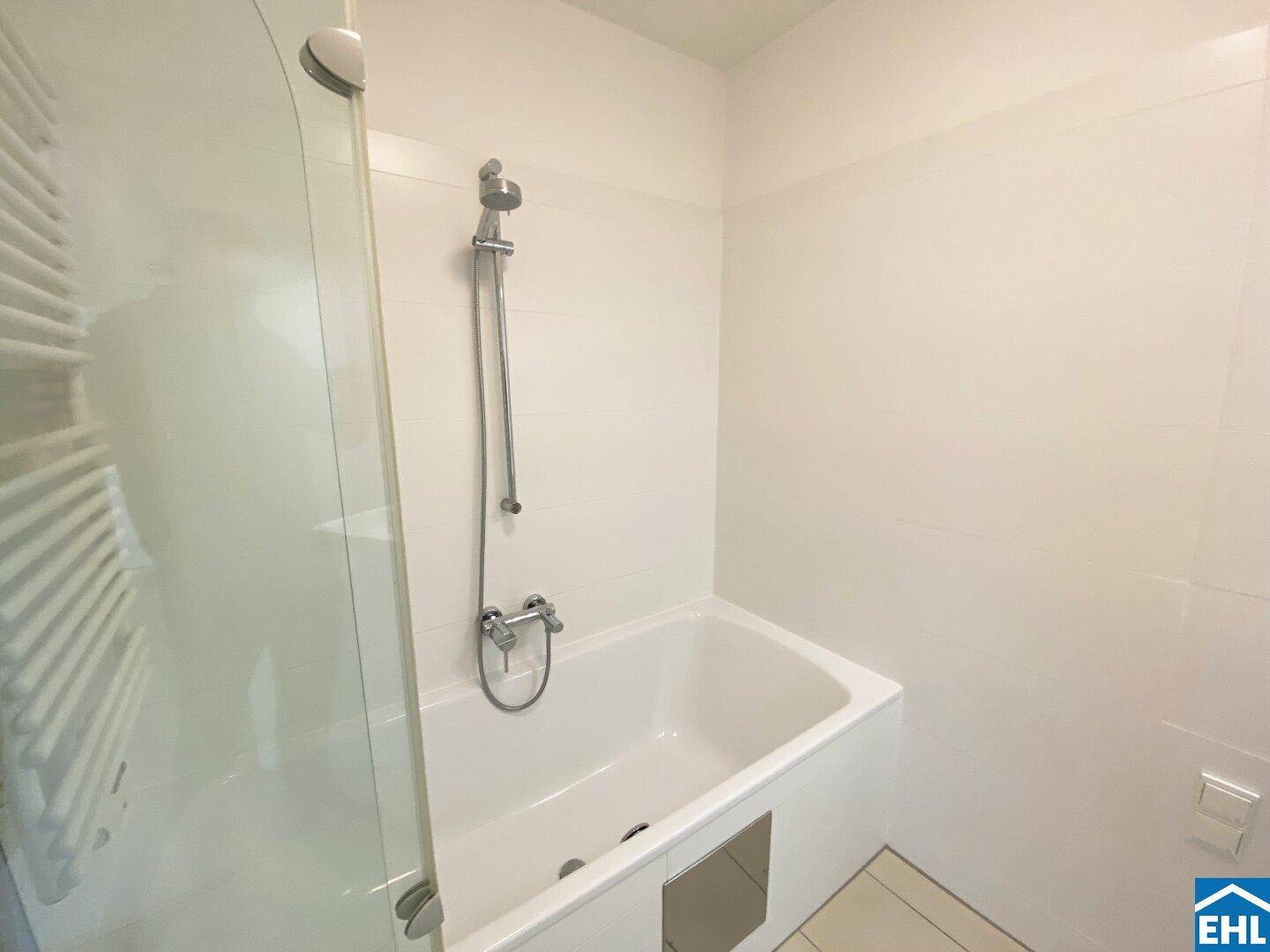 Badezimmer mit Badewanne, Duscharmatur und weißen Fliesen, funktional und sauber.