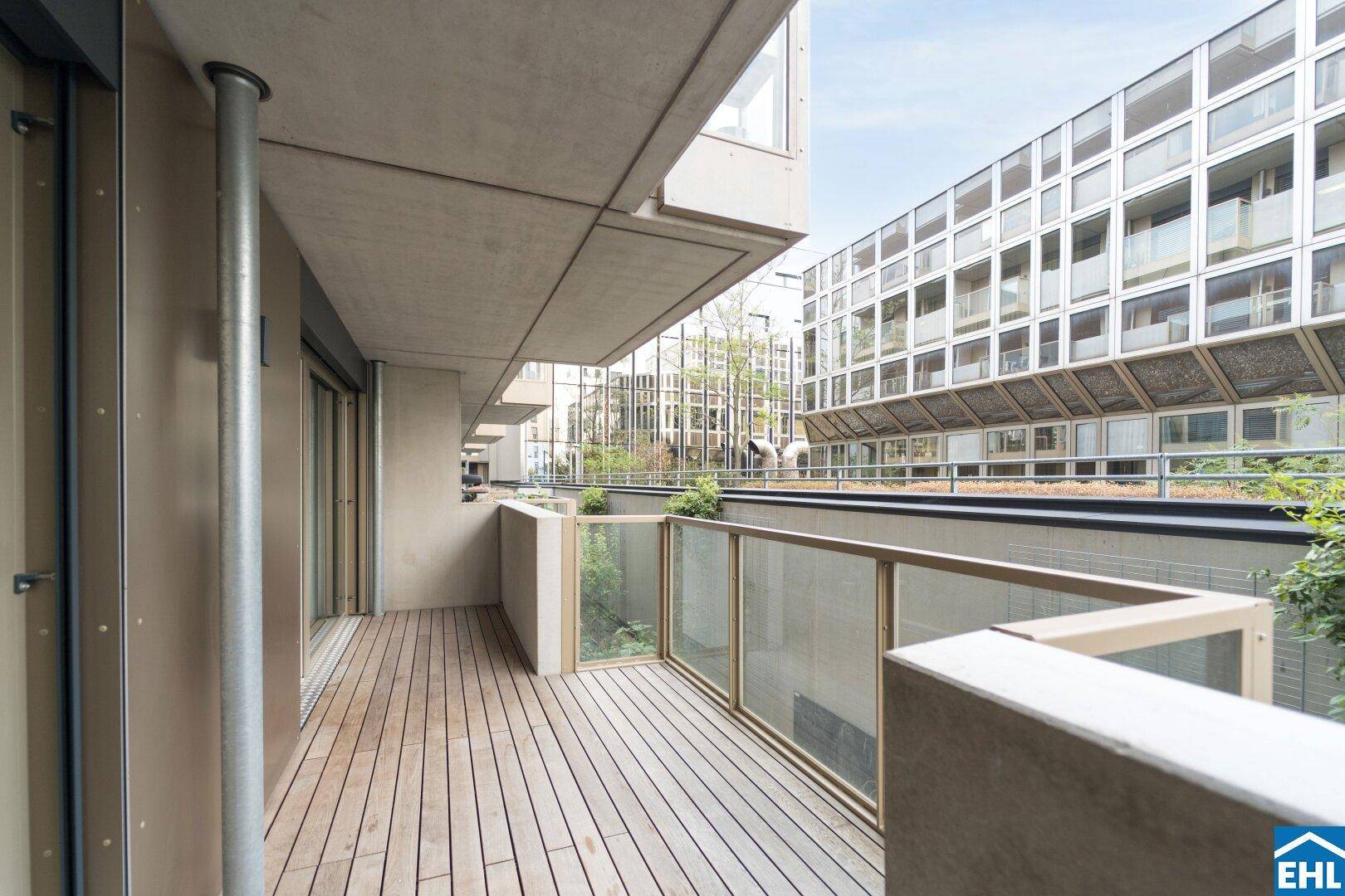 Langer Balkon mit Holzdielen und Glasbrüstung, bietet einen Blick auf die umliegenden Gebäude.