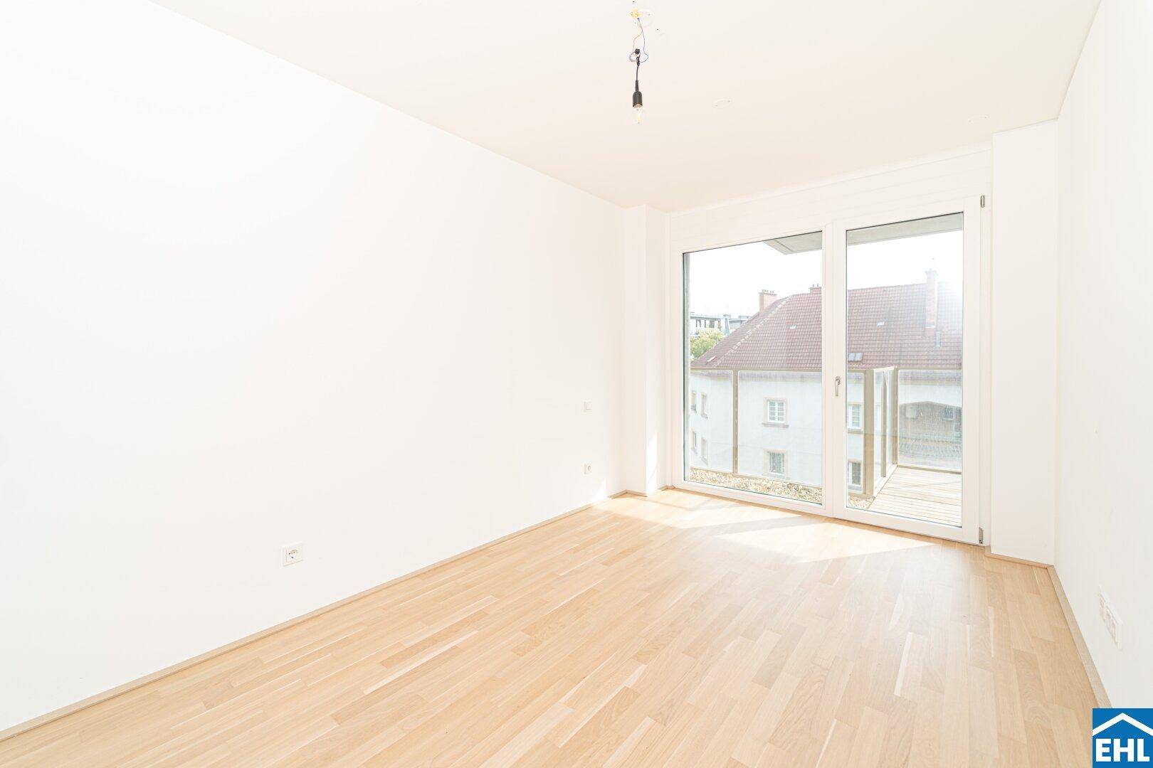 Heller Raum mit Parkettboden und großer Schiebetür, die Zugang zu einem Balkon bietet.