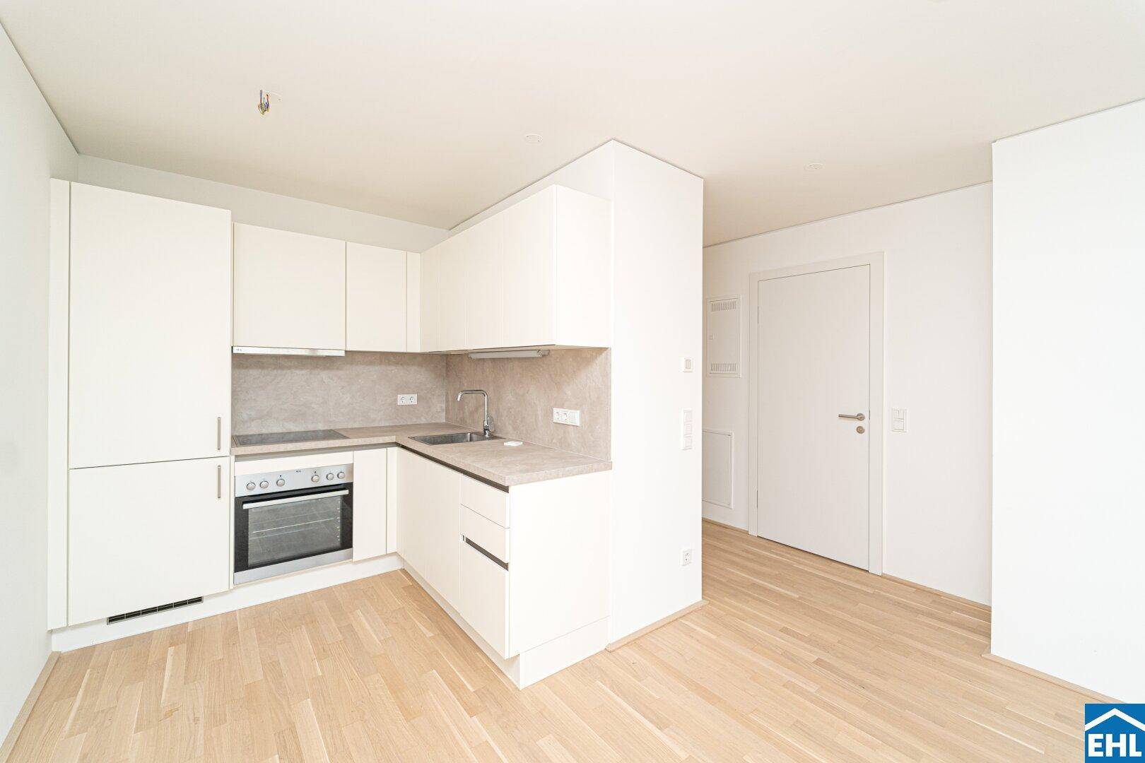 Moderne Einbauküche mit weißen Schränken, integriertem Backofen und hellem Parkettboden.
