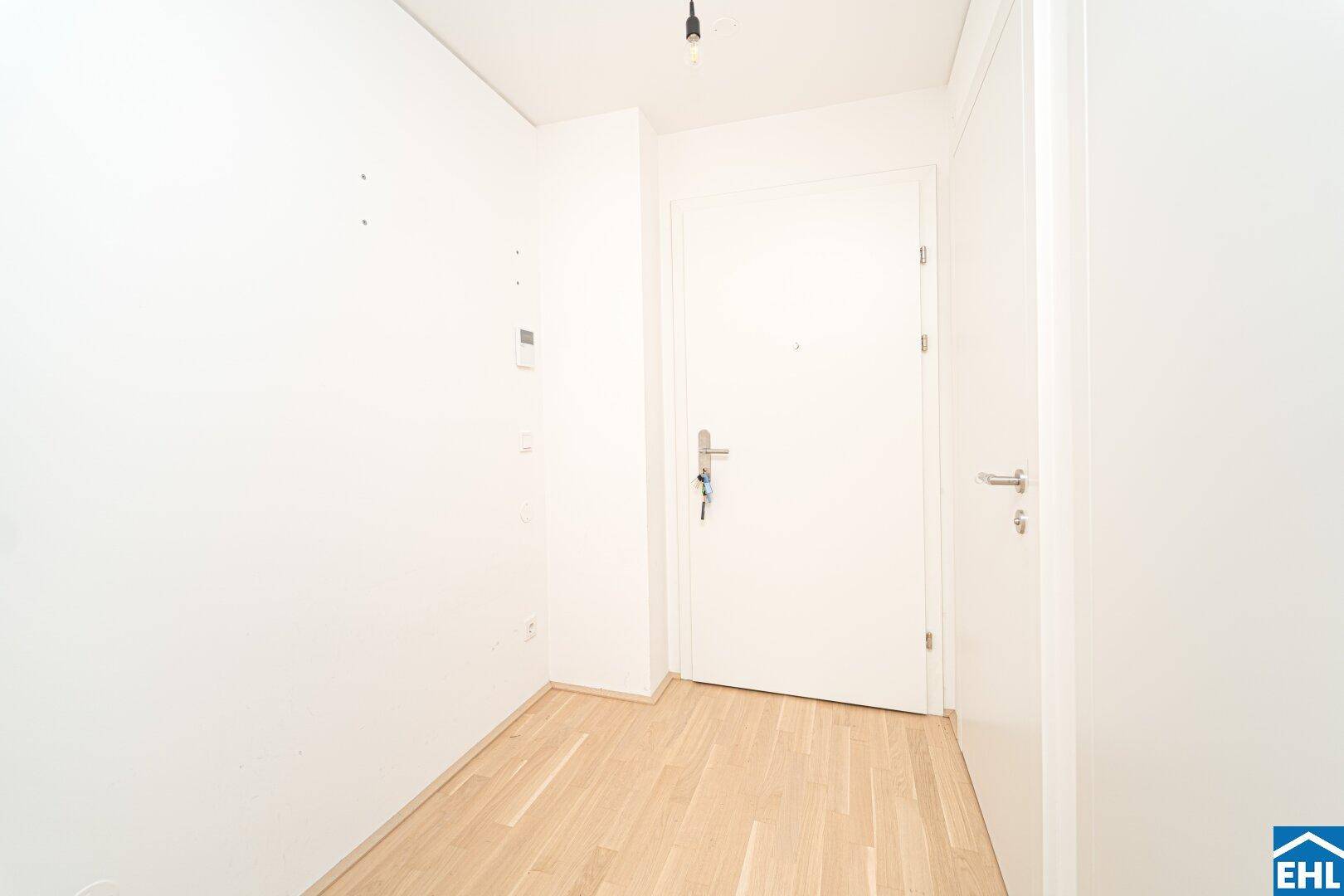 Heller Eingangsbereich mit Parkettboden und weißer Eingangstür, die in die Wohnung führt.