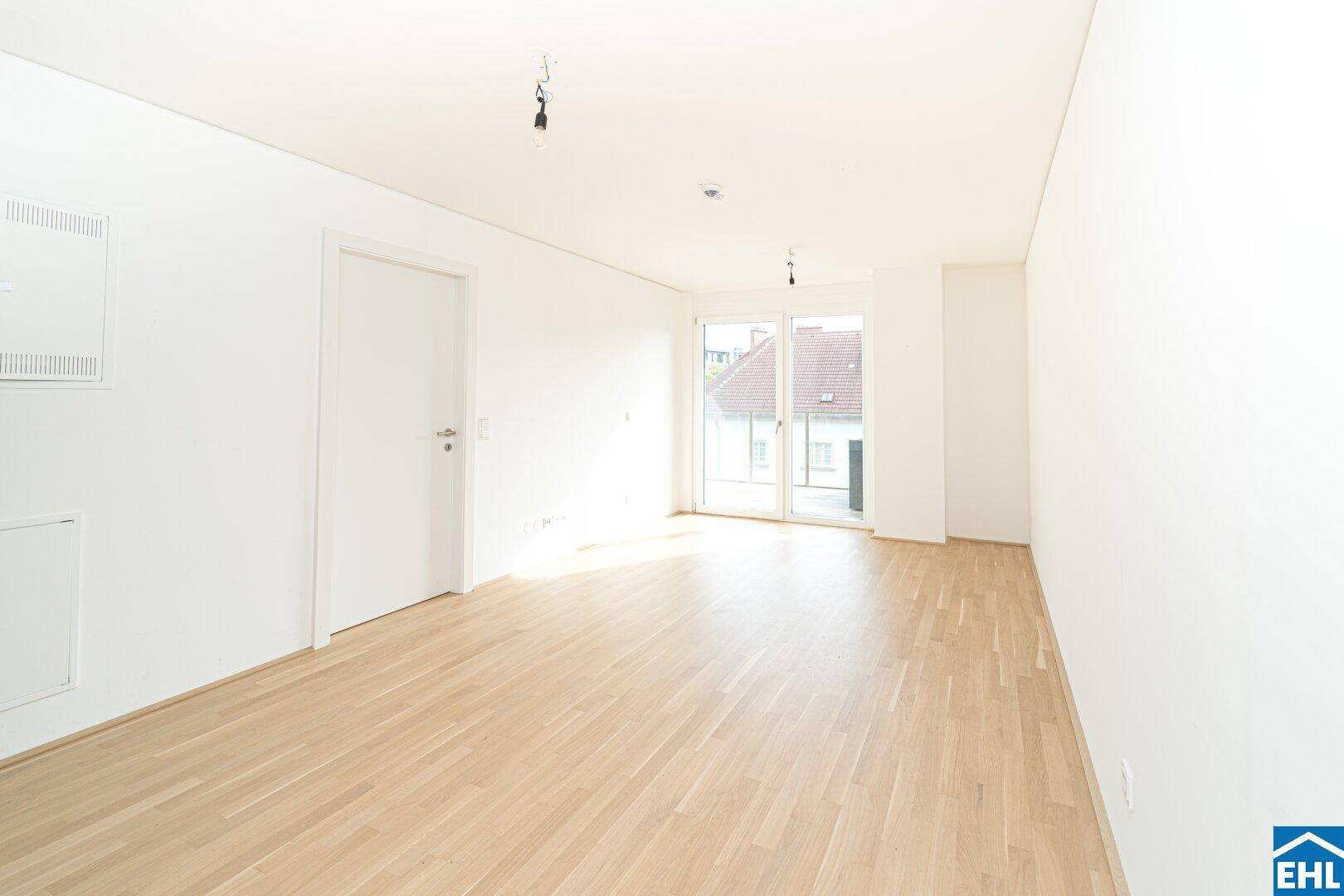 Großzügiger, heller Wohnbereich mit Parkettboden und Zugang zu einem Balkon durch große Fenster.