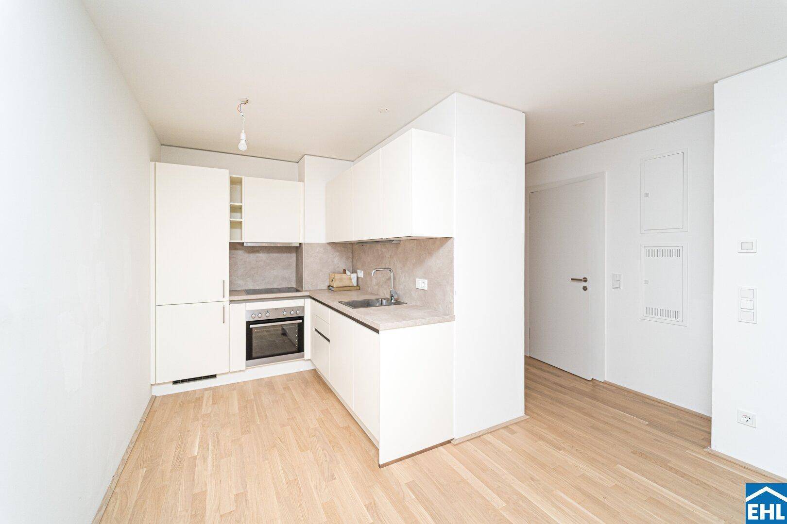Moderne, helle Einbauküche mit weißen Schränken, integriertem Backofen und Holzboden.