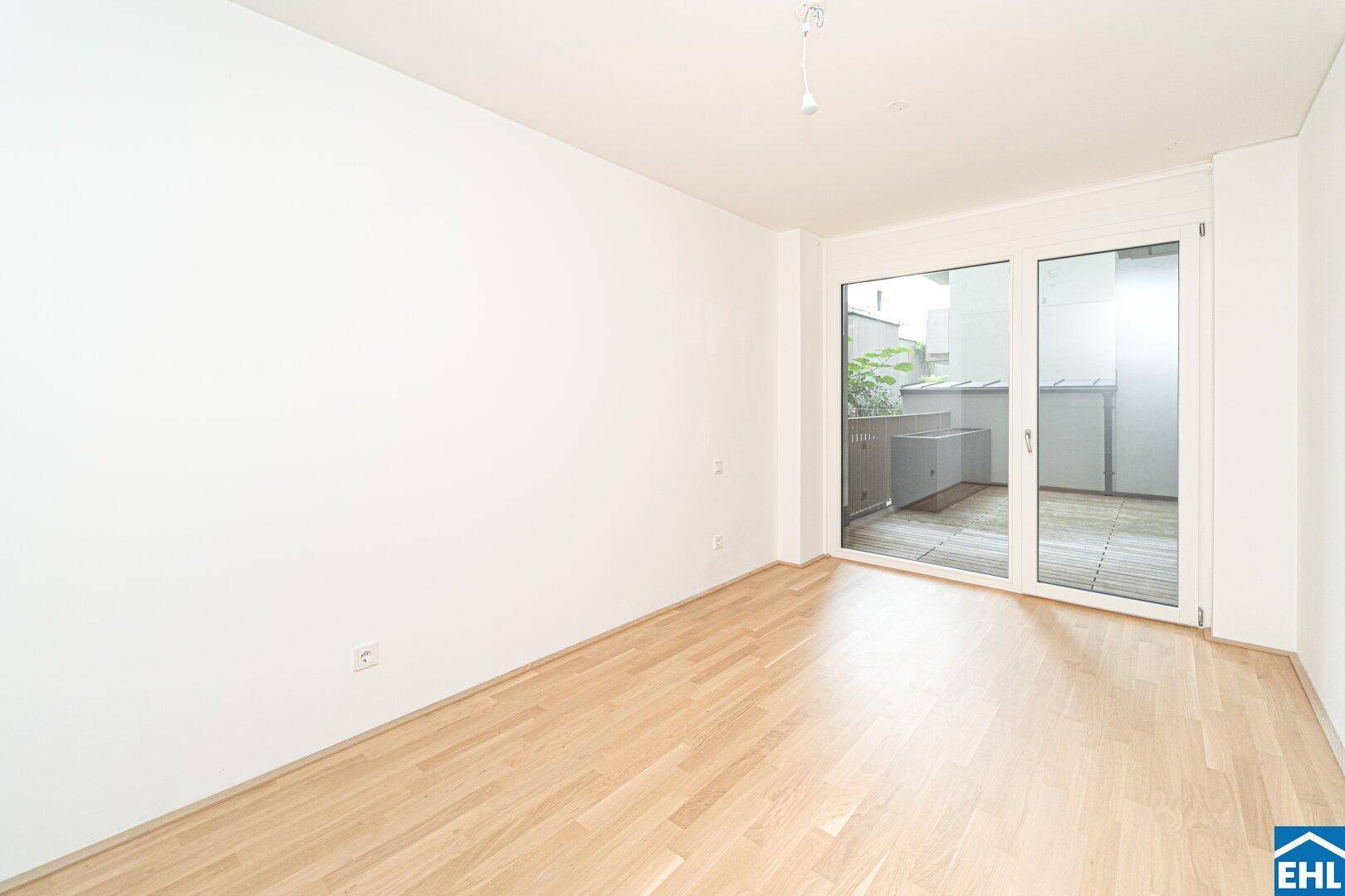 Helles Zimmer mit Holzboden und großen Schiebetüren, die direkt auf eine Terrasse führen.