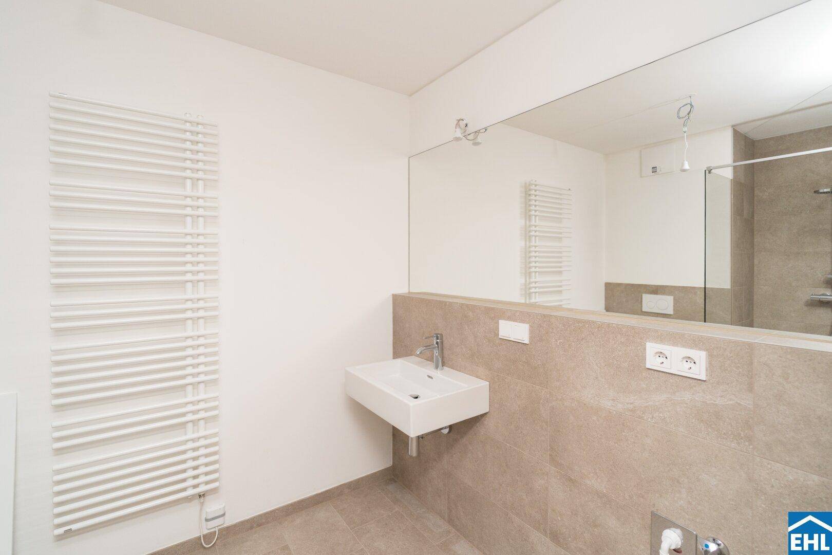 Modernes Badezimmer mit Wandwaschbecken, großem Spiegel, beheiztem Handtuchhalter und Dusche.