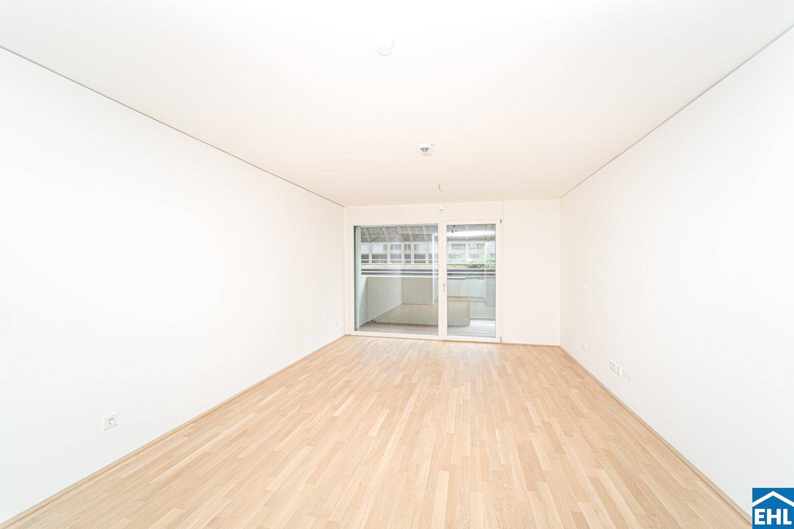 Heller, leerer Raum mit Holzboden und großer Glasschiebetür, die zu einem Außenbereich führt.