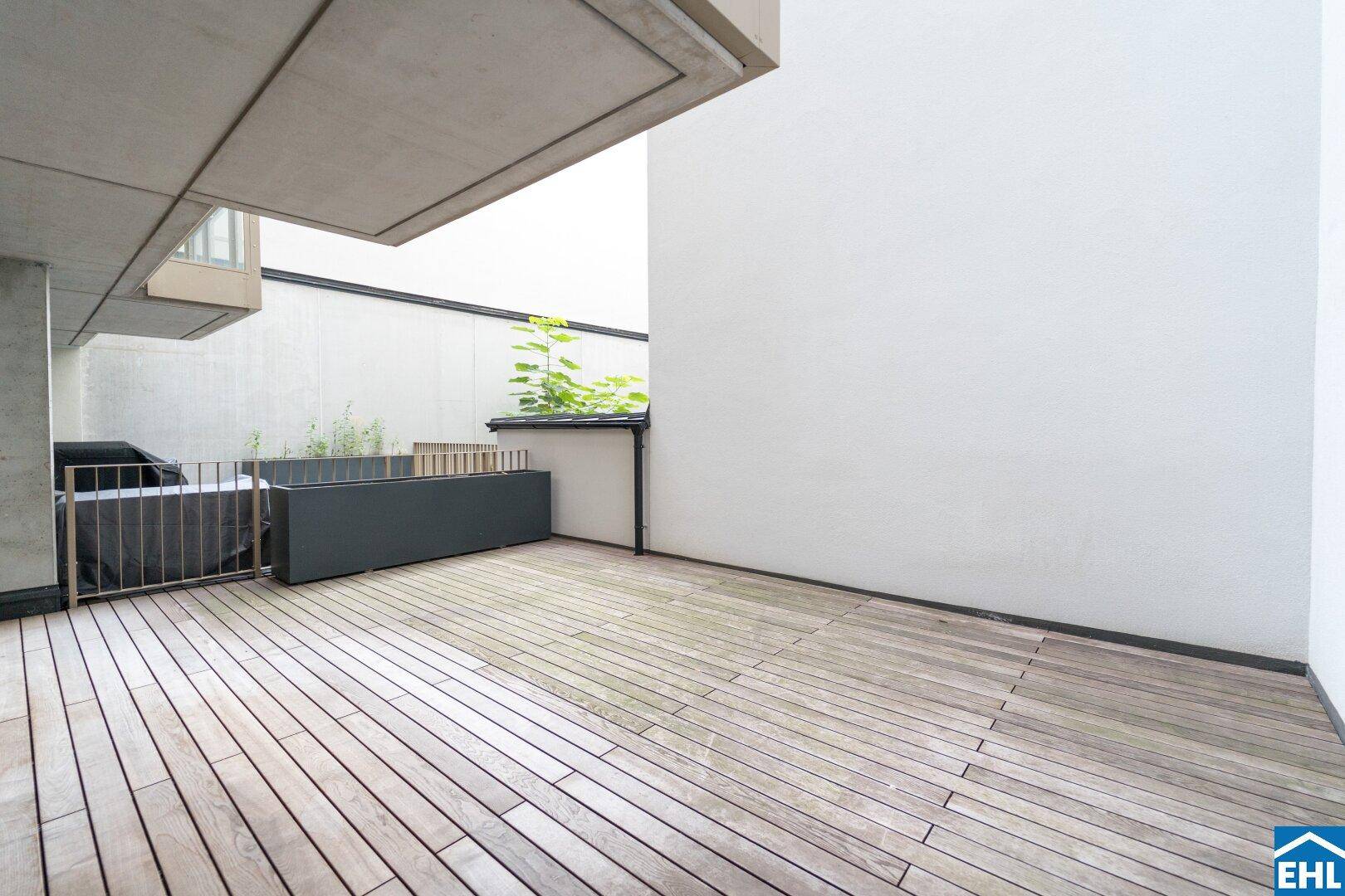 Geräumige Außenterrasse mit Holzbelag, umgeben von modernen Pflanzgefäßen und weißen Wänden.
