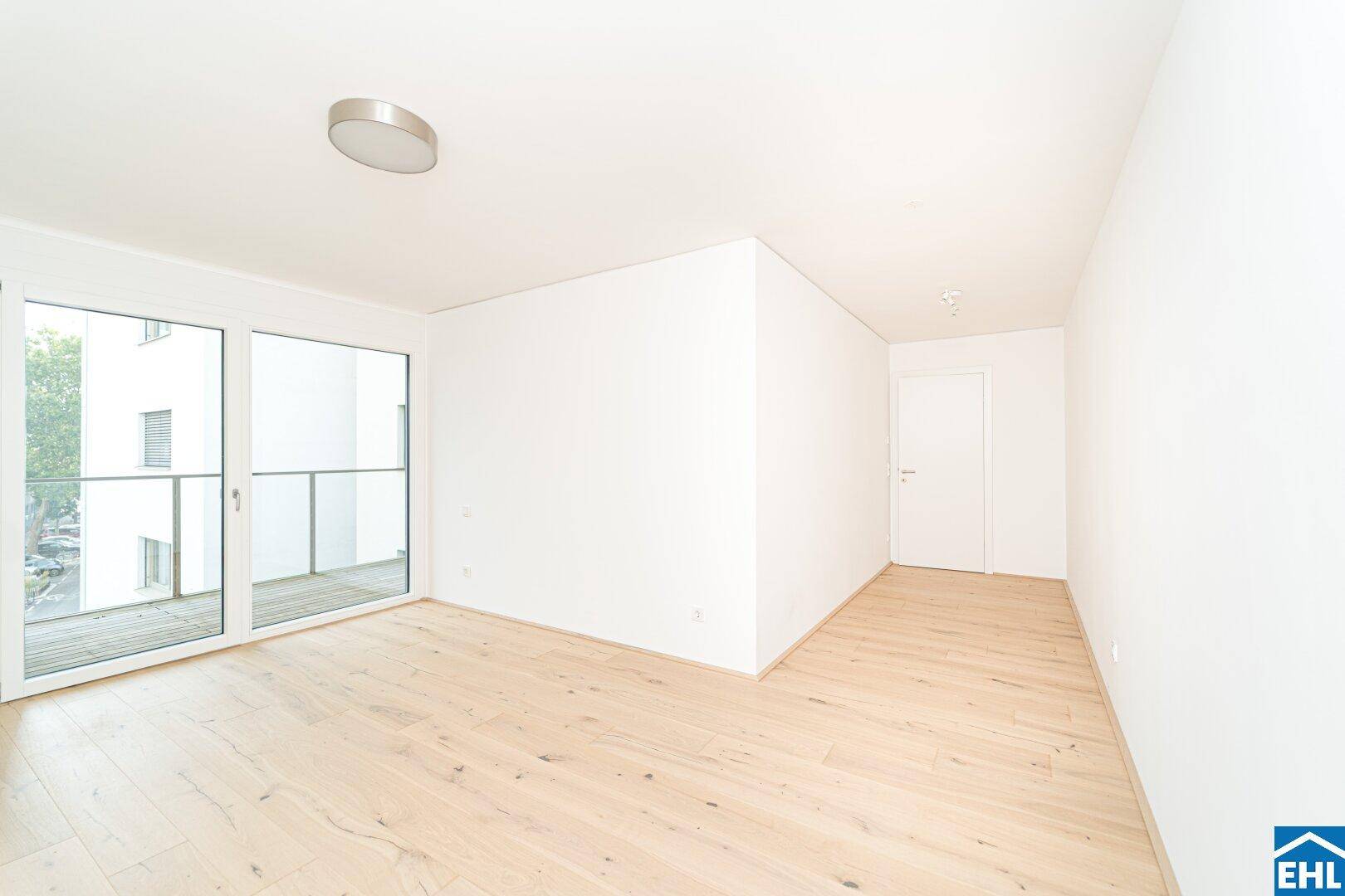 Geräumiges, helles Zimmer mit Holzboden und Zugang zu einem Balkon, ideal für ein Wohnzimmer.