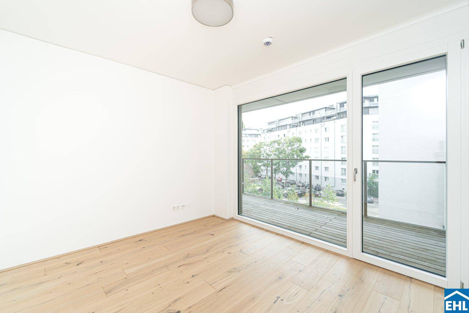 Lichtdurchflutetes Zimmer mit Holzboden und breitem Balkonzugang, bietet einen Blick auf die Stadt.