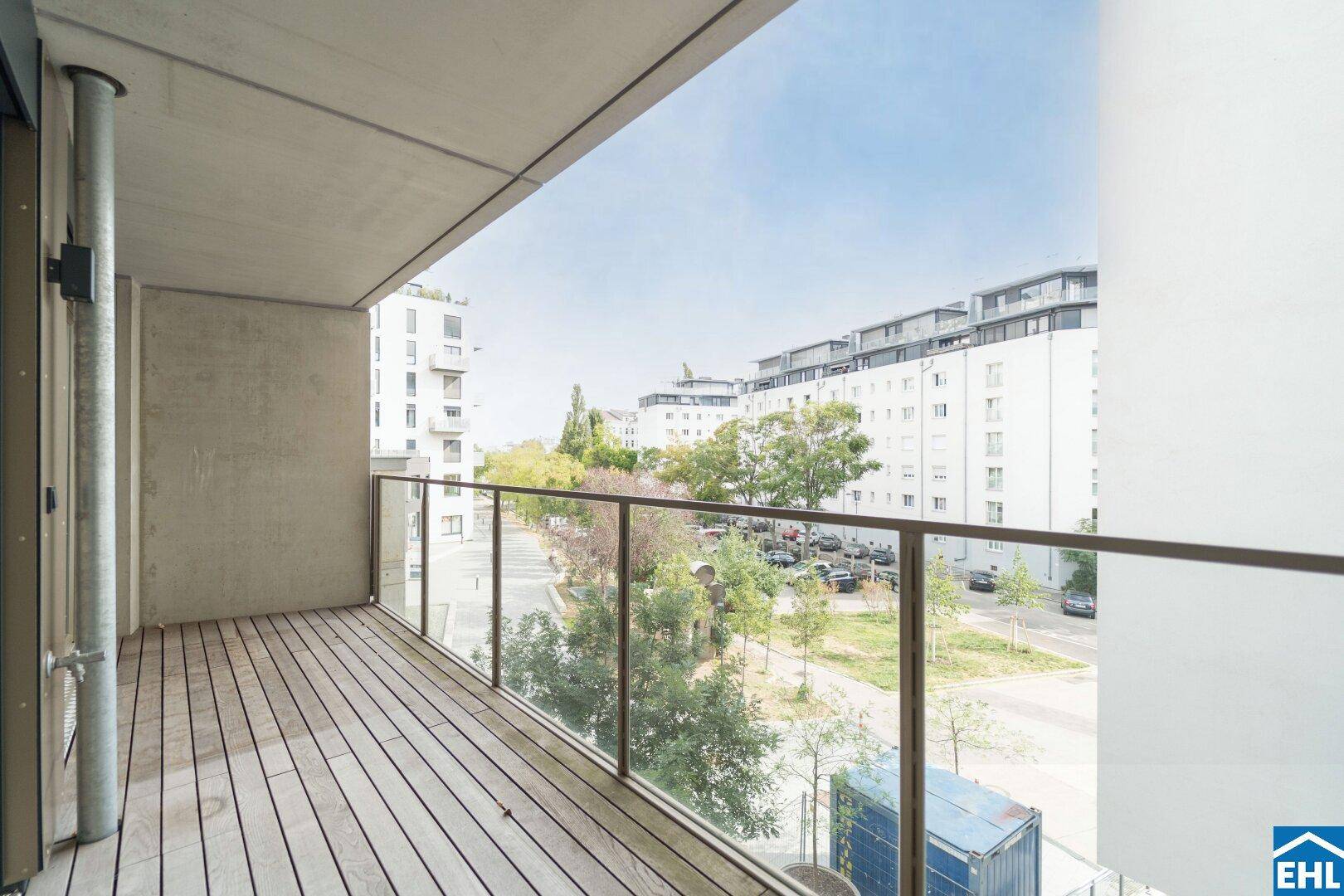 Geräumiger Balkon mit Holzbelag und Glasgeländer, bietet einen Ausblick auf die umliegende Stadt.