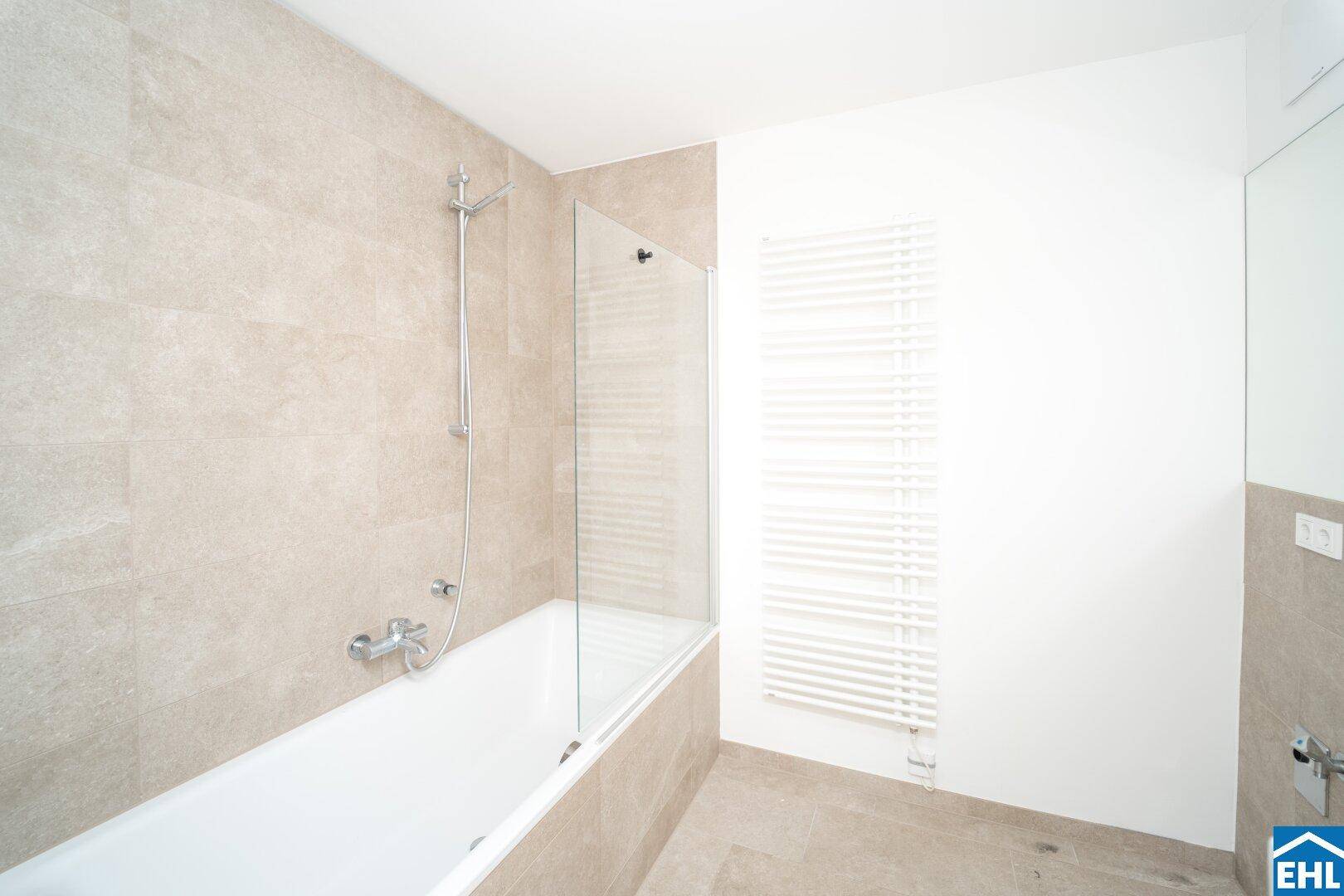 Helles Badezimmer mit Badewanne, Duschabtrennung aus Glas und Handtuchheizkörper.