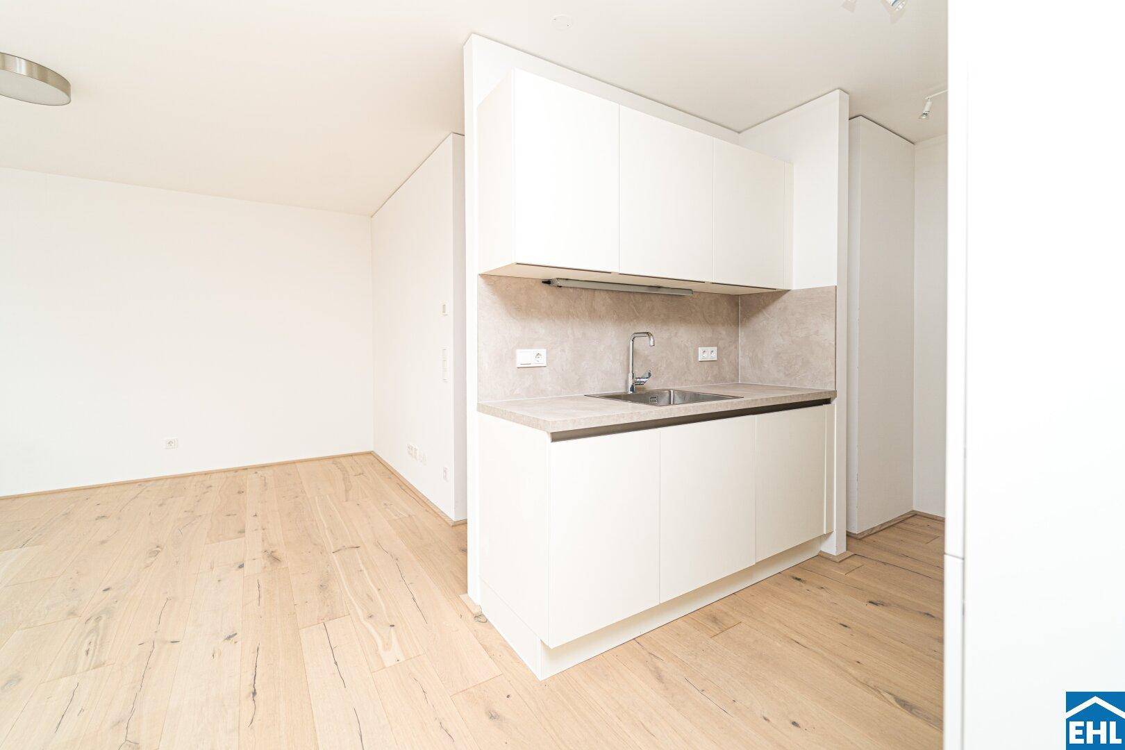 Moderne Küchenzeile mit weißen Schränken, Spüle und heller Arbeitsplatte, funktional und kompakt.