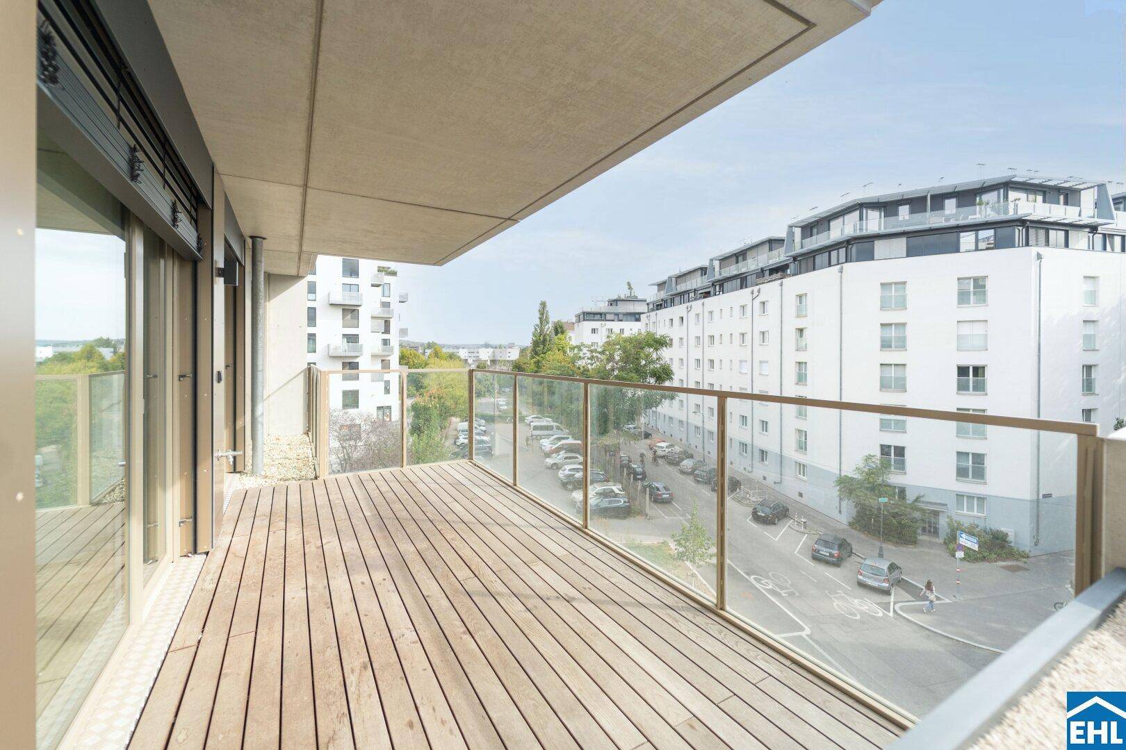 Geräumiger Balkon mit Holzboden, Glasgeländer und Blick auf die Stadt.