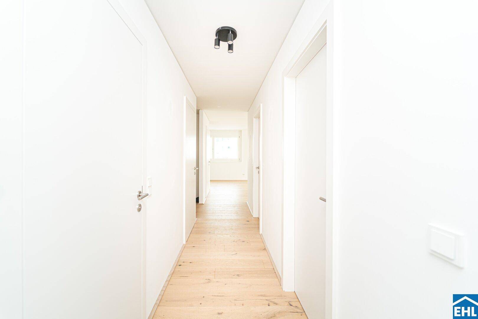 Heller Flur mit Holzboden und weißen Türen, der zu weiteren Räumen führt.