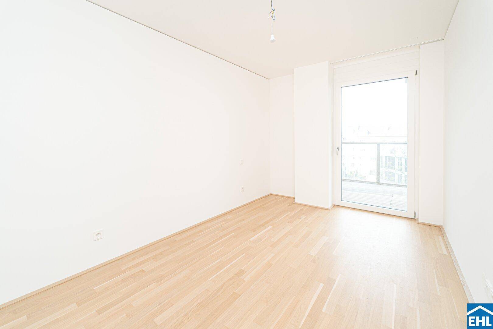 Leeres Schlafzimmer mit hellem Parkettboden und direktem Zugang zu einem sonnigen Balkon.
