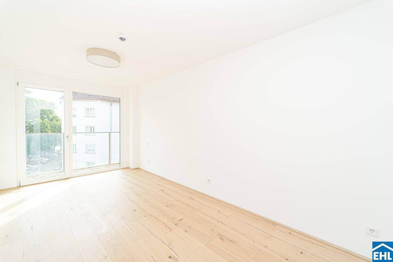 Helles, unmöbliertes Zimmer mit Holzboden und Zugang zu einem französischen Balkon.
