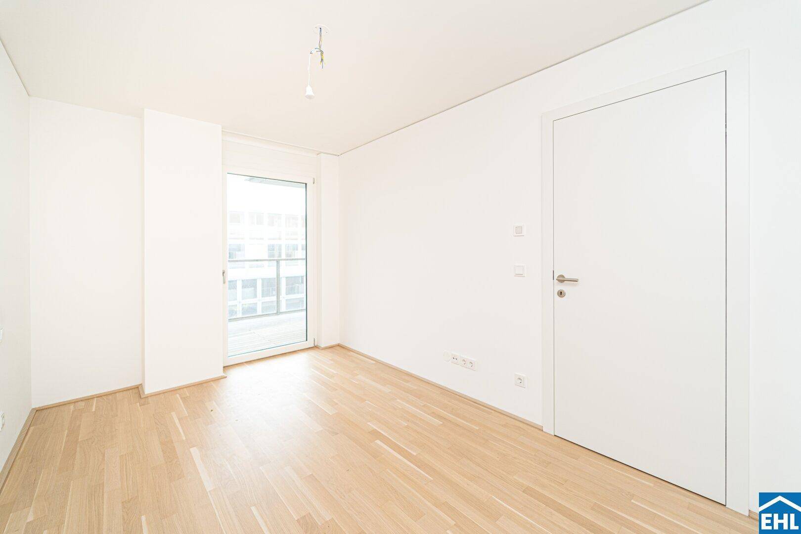 Unmöbliertes Zimmer mit Parkettboden und einer Tür, die zu einem Außenbereich führt.