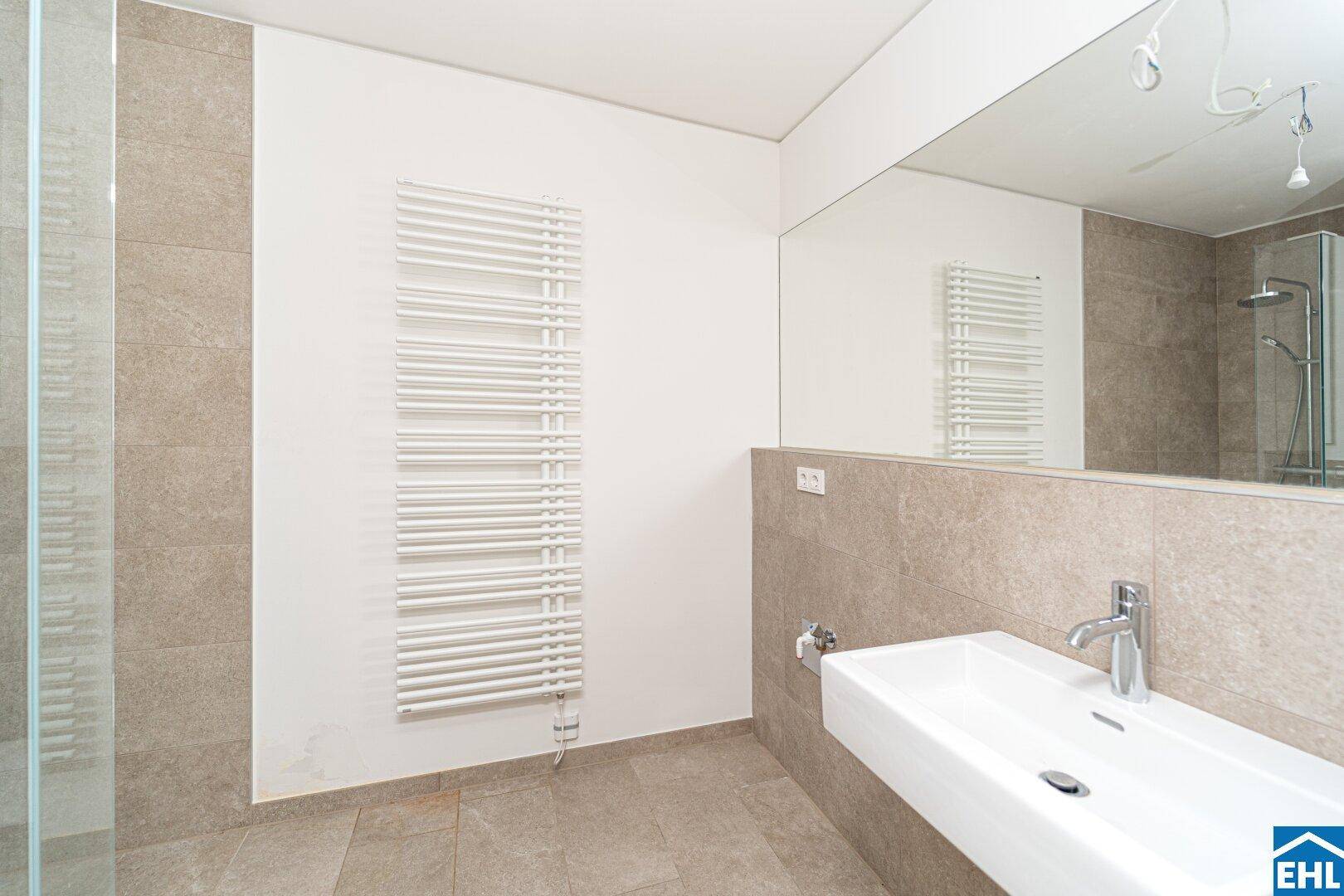 Modernes Badezimmer mit großem Spiegel, schwebendem Waschbecken und beheiztem Handtuchhalter.