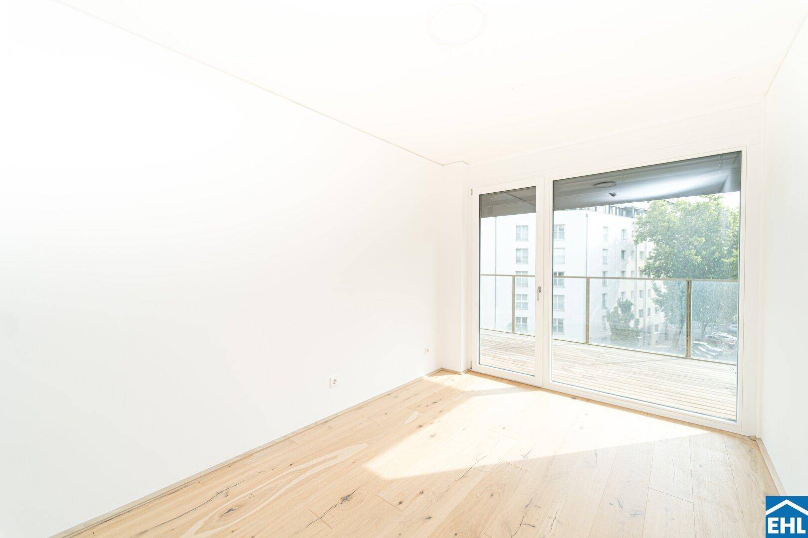Lichtdurchflutetes Zimmer mit Holzboden und großem Fenster zum Balkon.