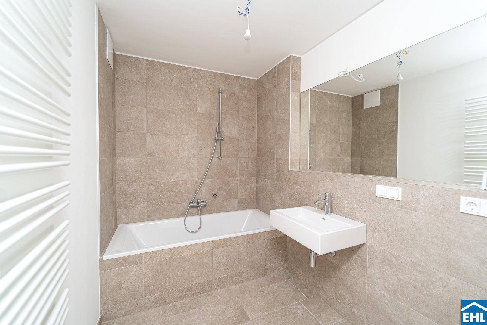 Modernes Badezimmer mit beigefarbenen Fliesen, Badewanne mit Duschfunktion und wandhängendem Waschbecken.