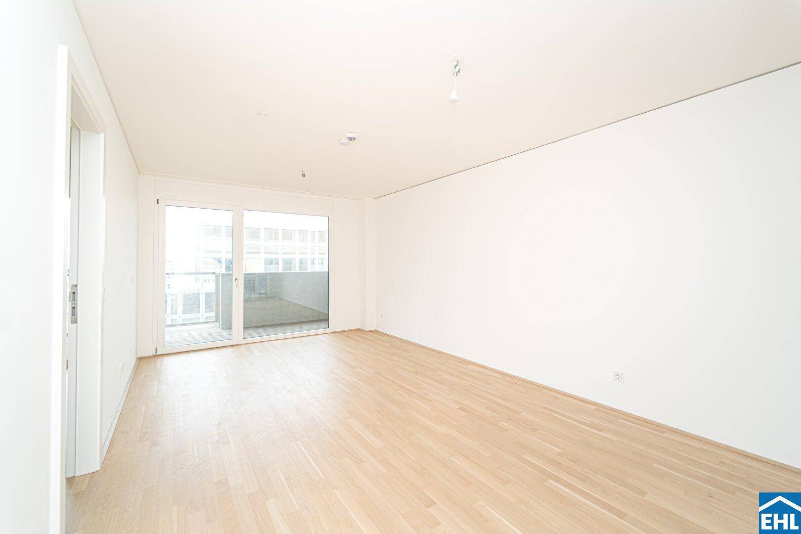 Großzügiger Wohnraum mit Parkettboden und breiter Schiebetür zum Balkon, bietet viel Tageslicht.