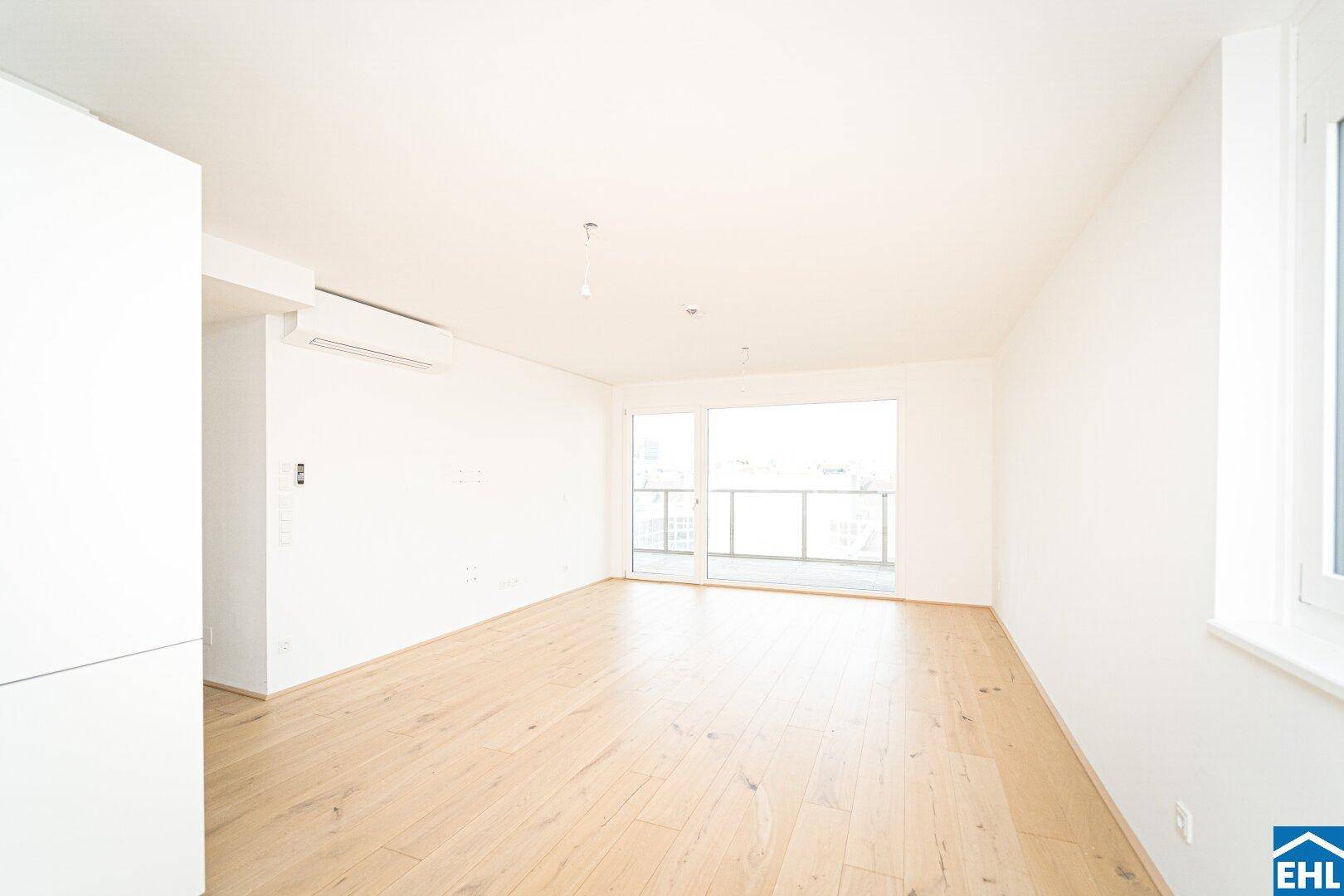 Geräumiger, heller Raum mit Holzboden, großen Fenstern und Zugang zu einem Balkon.