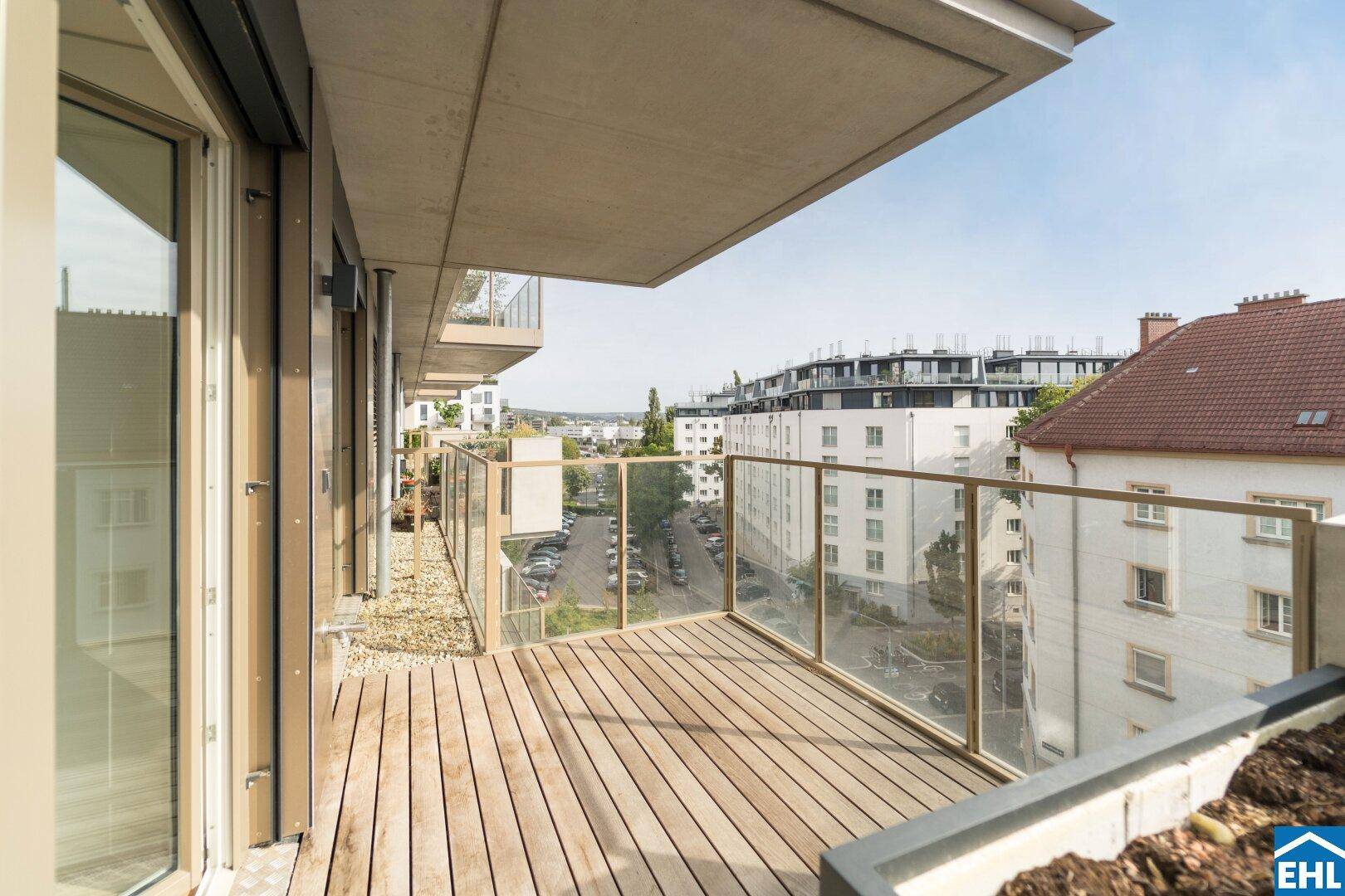 Heller Balkon mit Holzfußboden und Glasgeländer, bietet einen weiten Blick über die Stadtlandschaft.