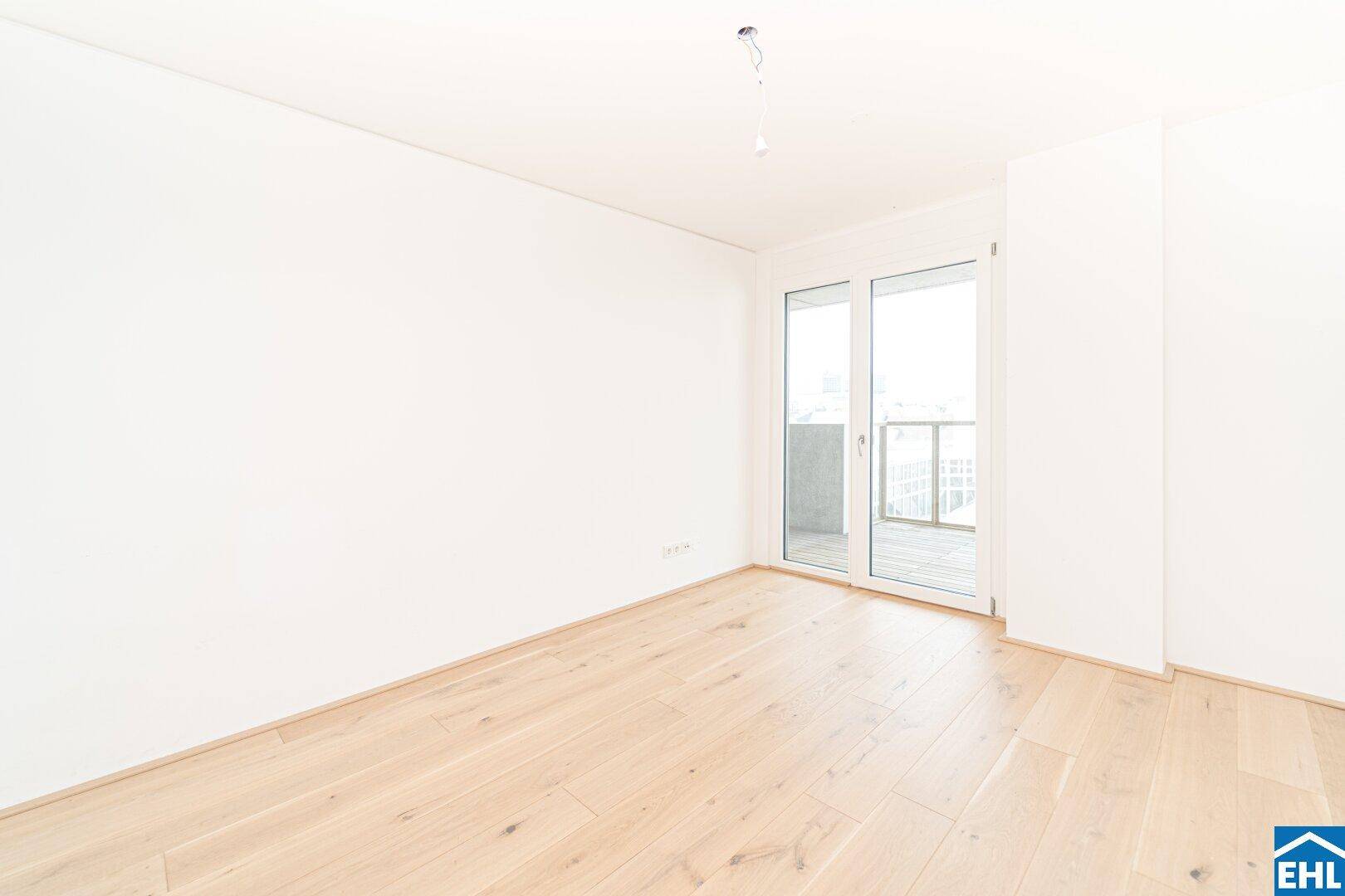 Lichtdurchflutetes Zimmer mit Holzboden und großen Fenstern, die auf einen Balkon führen.